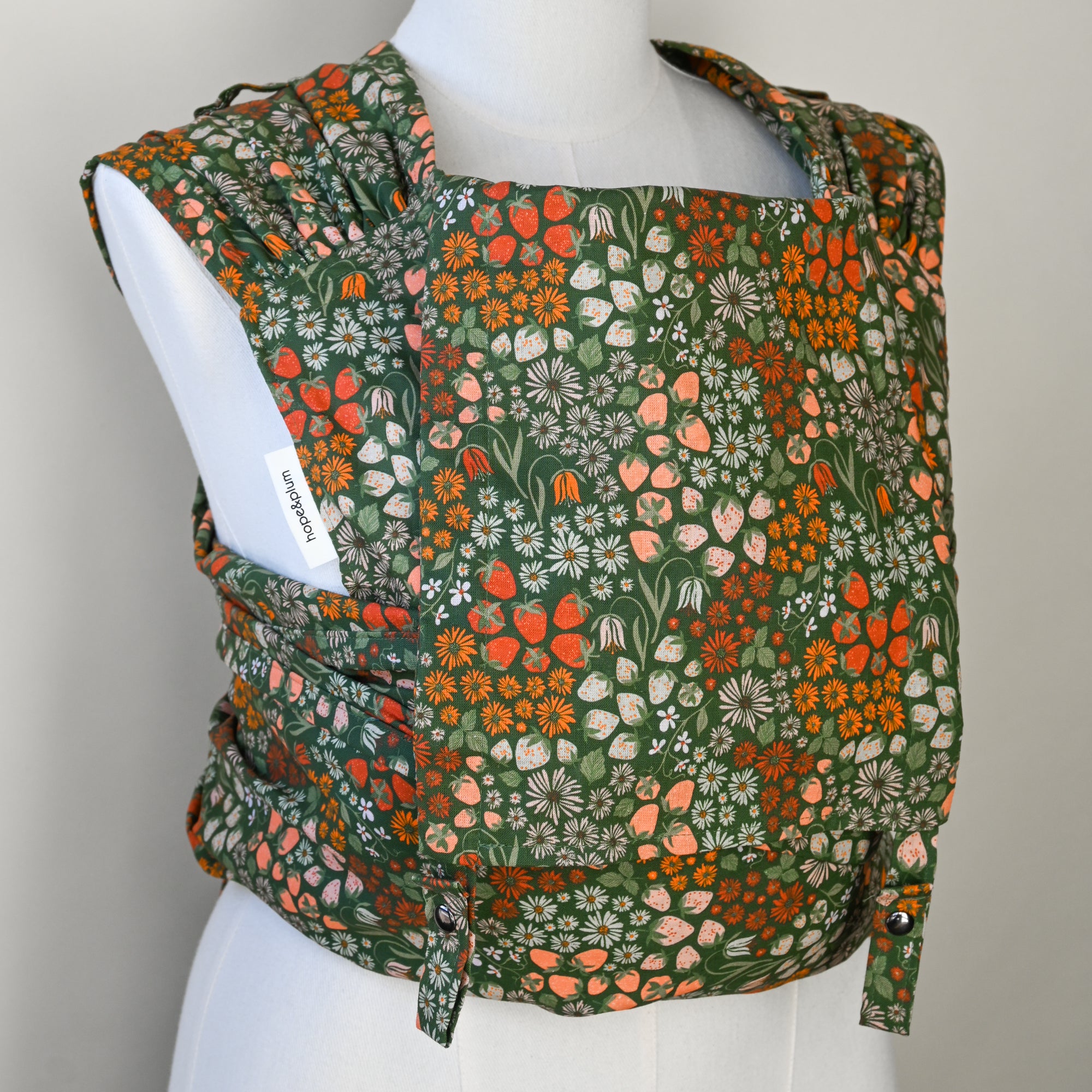Floral strawberry patterned baby carrier on a mannequin against a plain background
