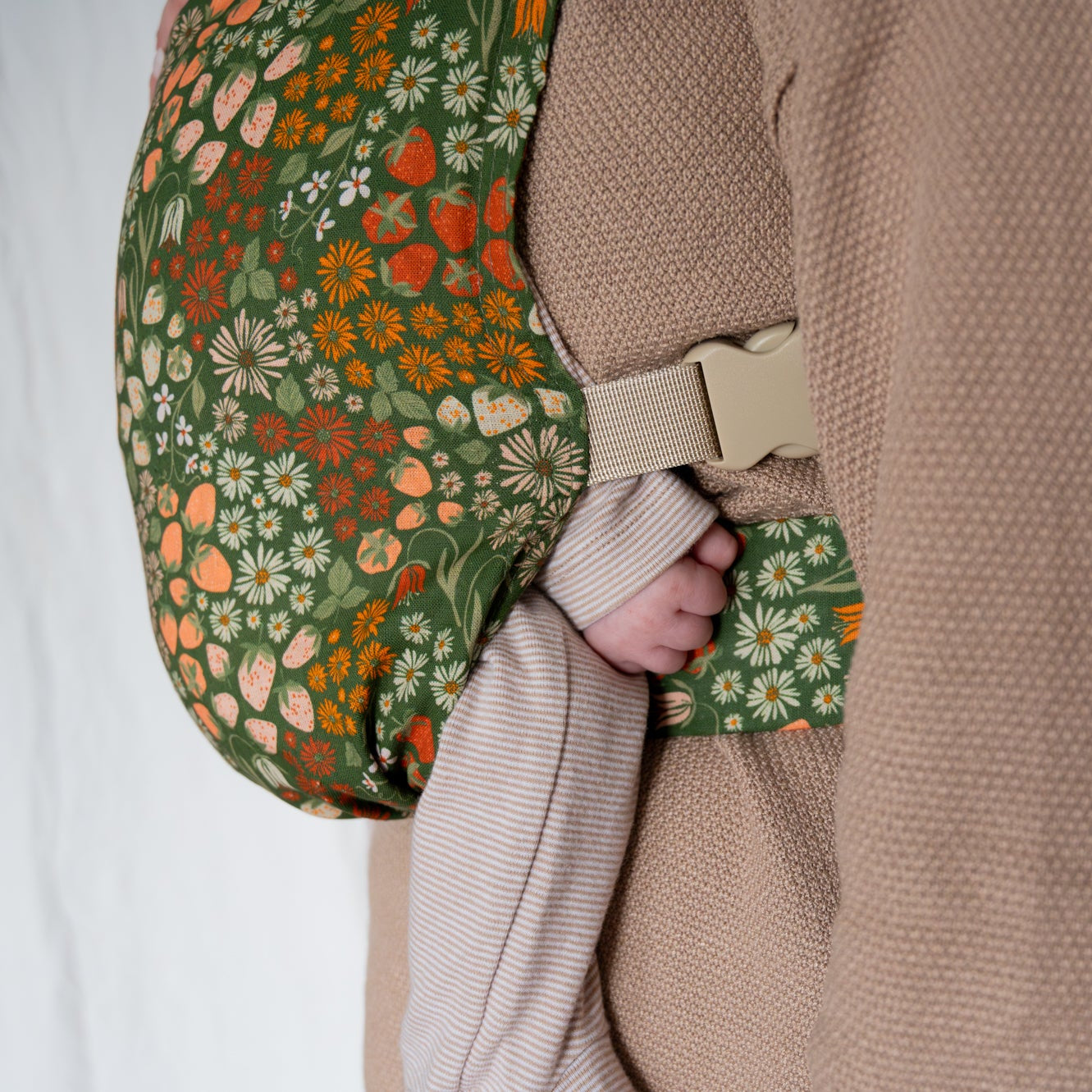 Person holding a floral and strawberry-patterned newborn carrier with a neutral background