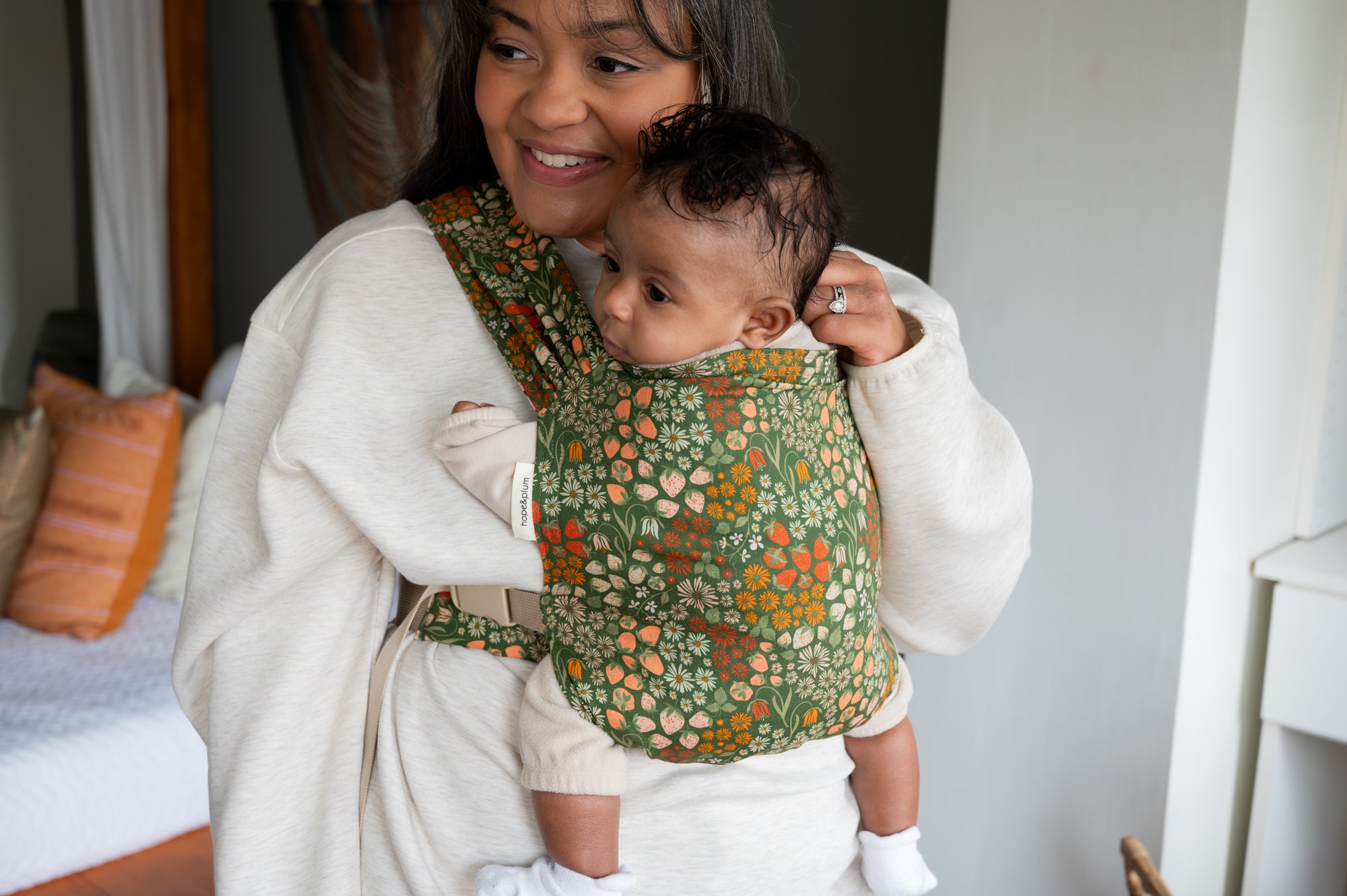 woman with black hair holding a baby in a strawberry printed carrier