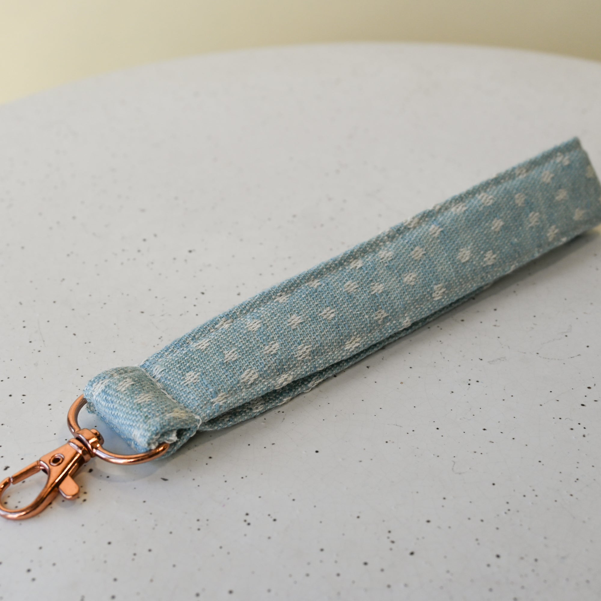 Light blue and white polka dot fabric keychain with rose gold clasp on a white surface