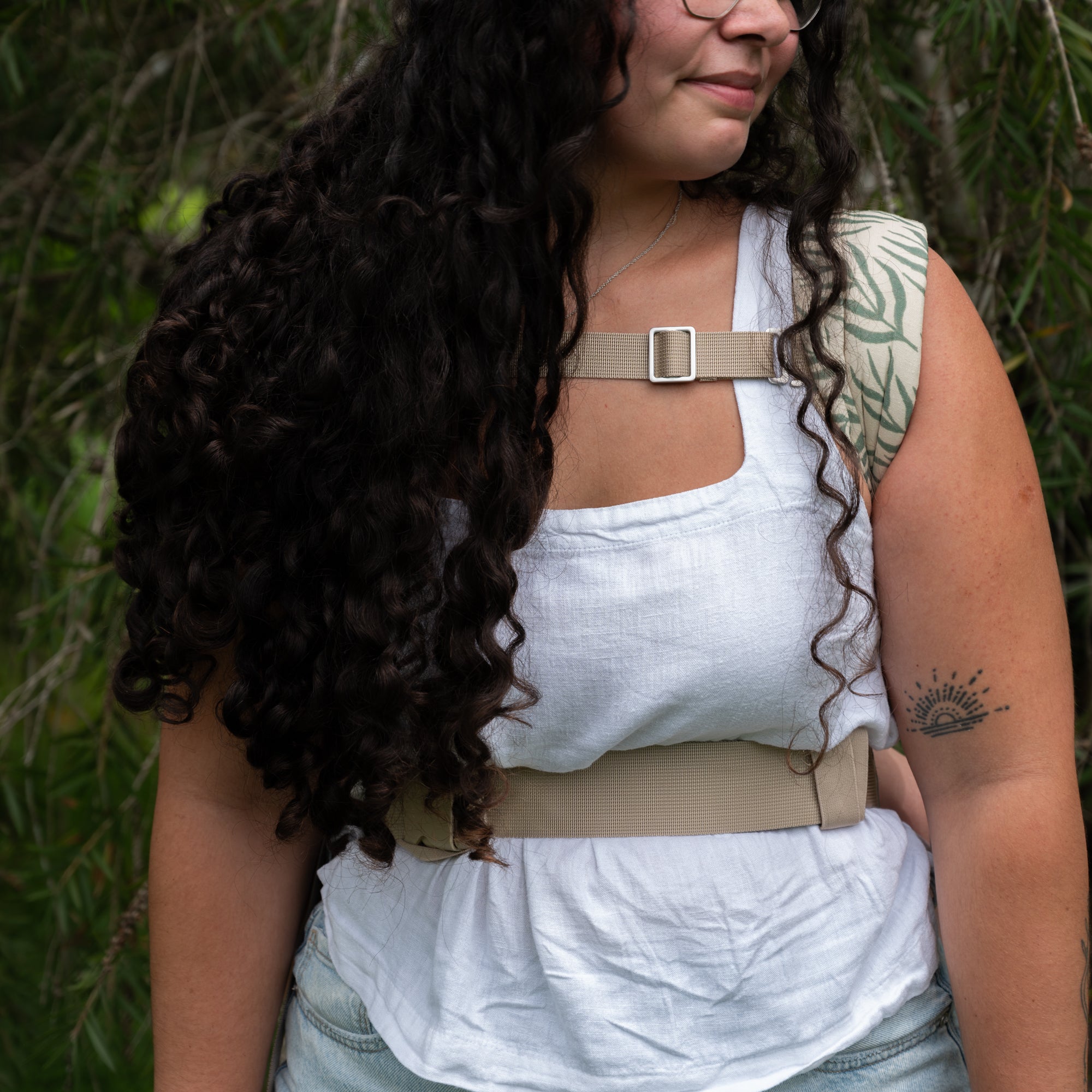Woman wearing a white top with a beige strap over her shoulder against a green leafy background