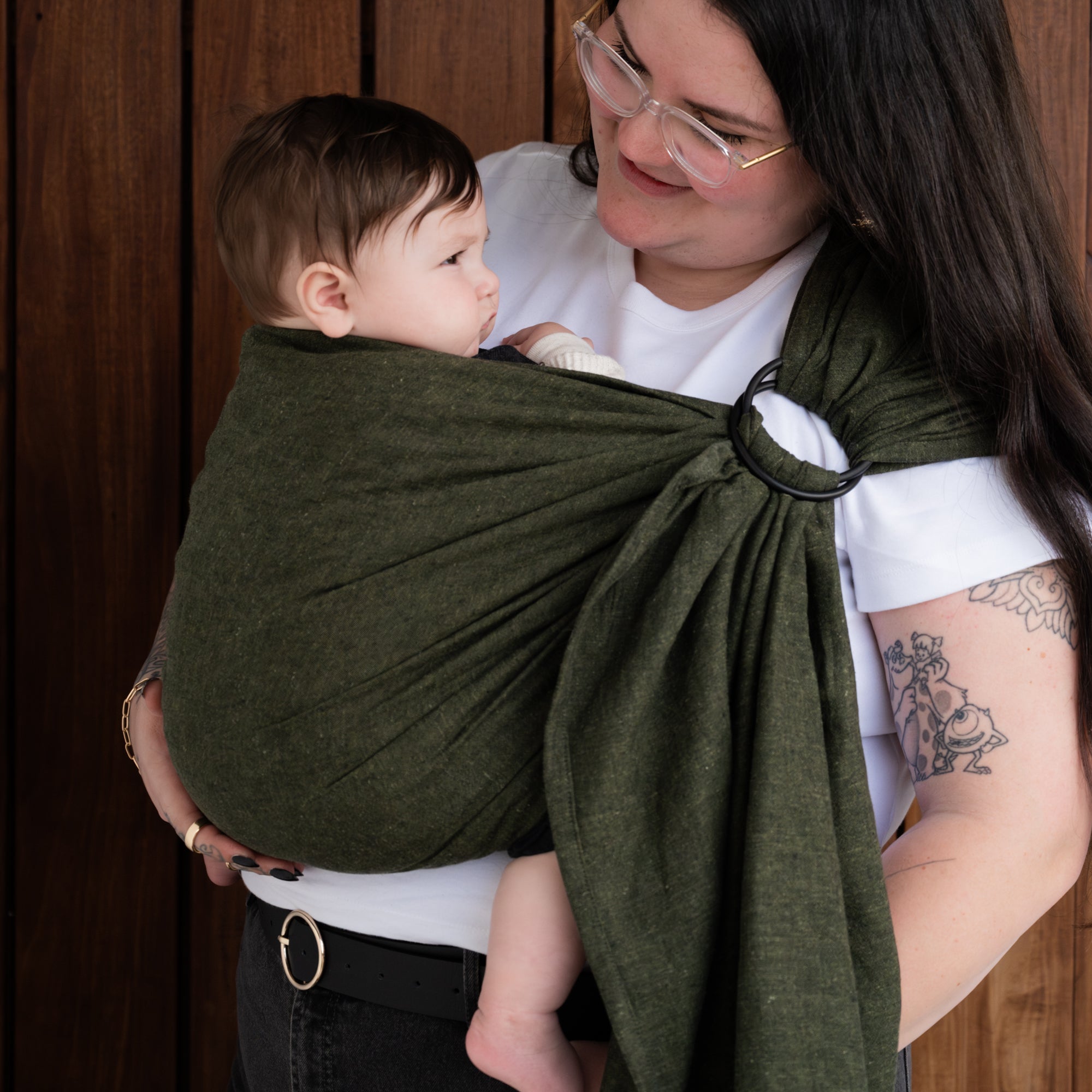 Woman holding a baby in a green sling against a wooden background