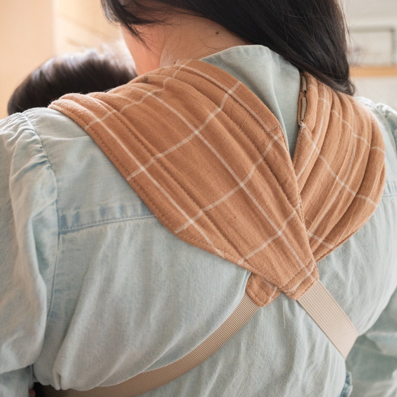 Woman holding a baby in a brown baby carrier with a white grid.