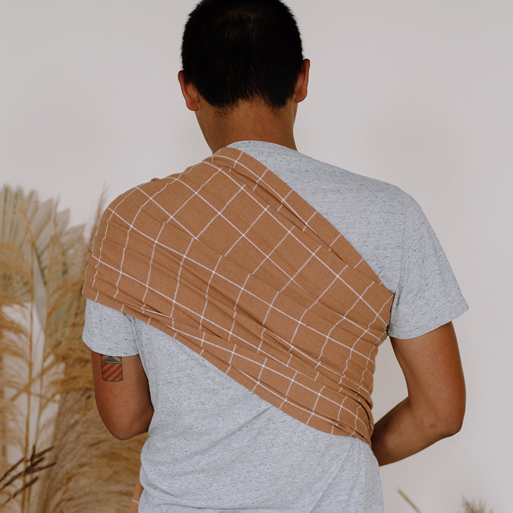 Person wearing a brown grid-patterned wrap over a gray shirt against a neutral background