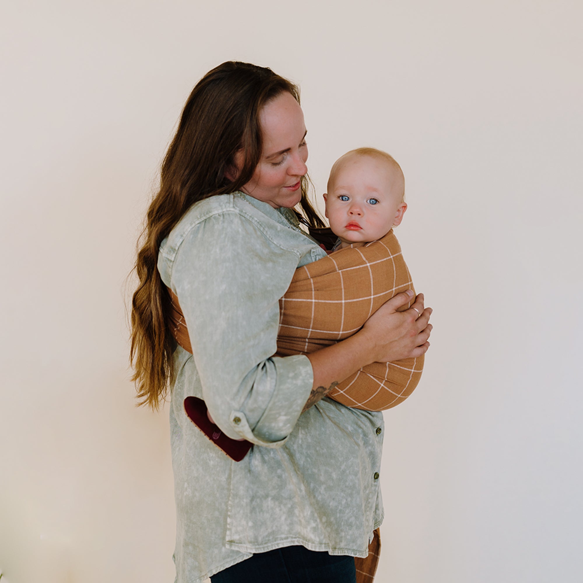 Woman holding a baby in a sling against a plain background