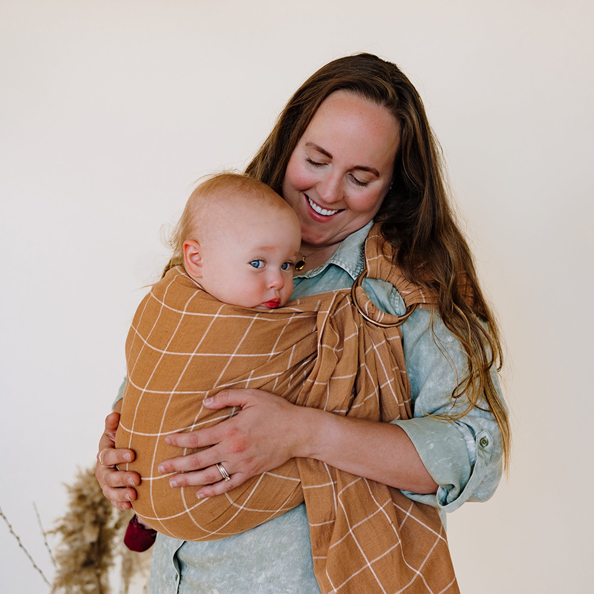 Woman holding a baby wrapped in a brown checkered wrap against a white background