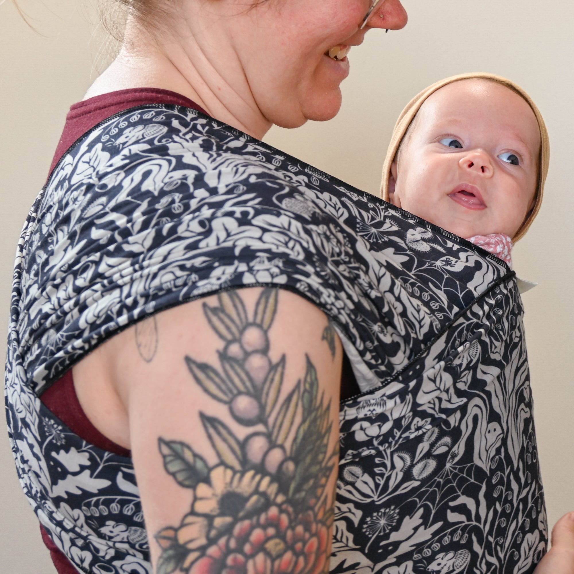 Person holding a baby in a floral-patterned sling against a neutral background