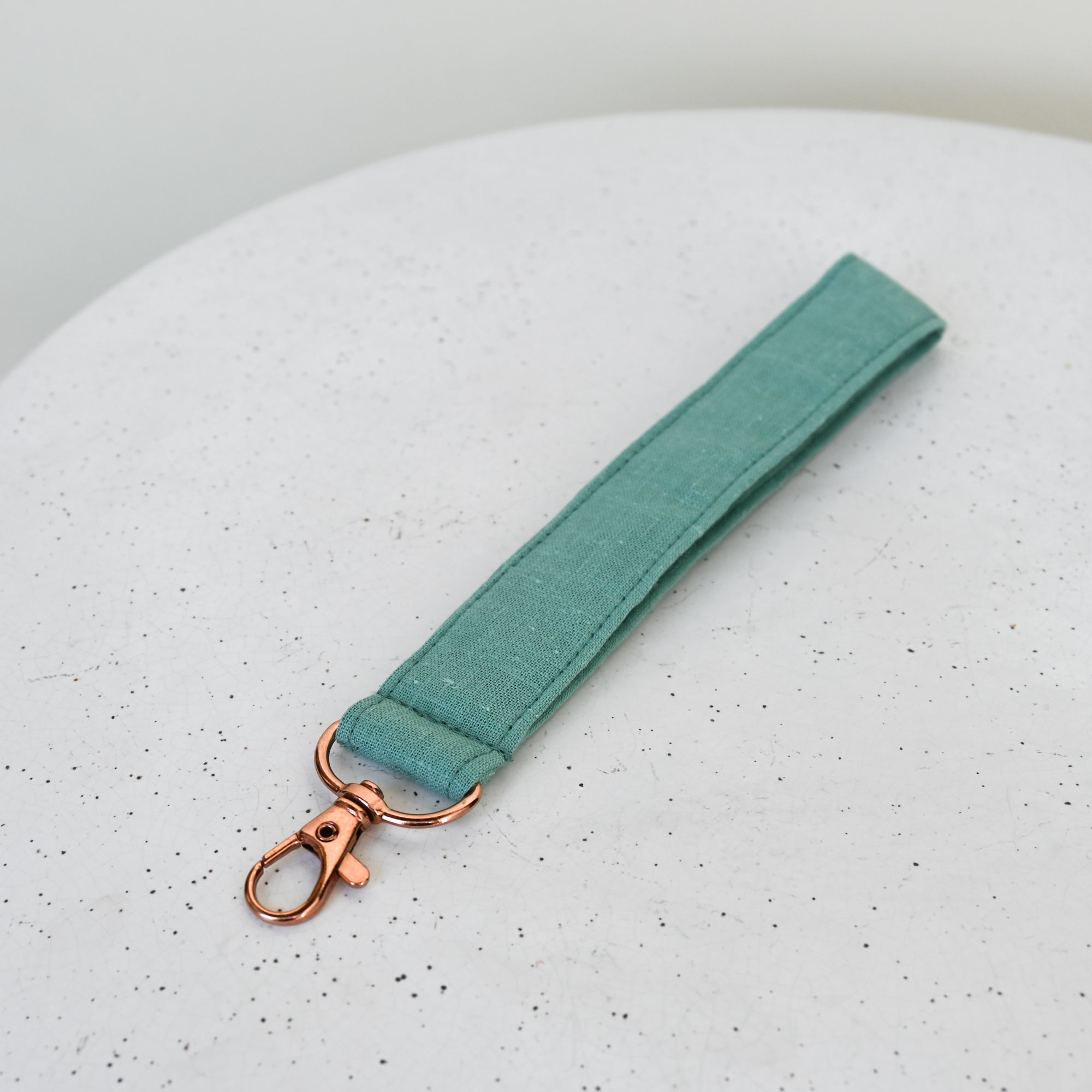 green fabric keychain strap with rose gold clasp on a speckled gray surface