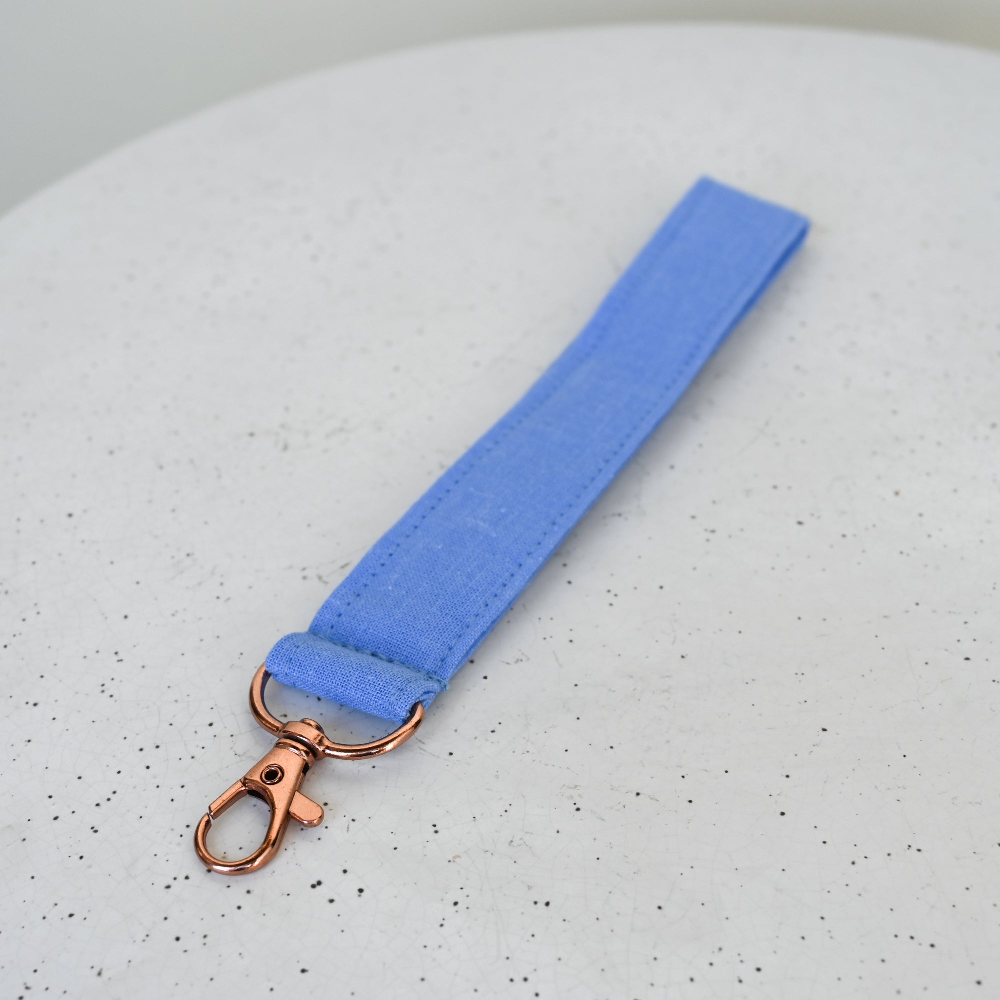 Blue keychain strap with rose gold clasp on a speckled gray background