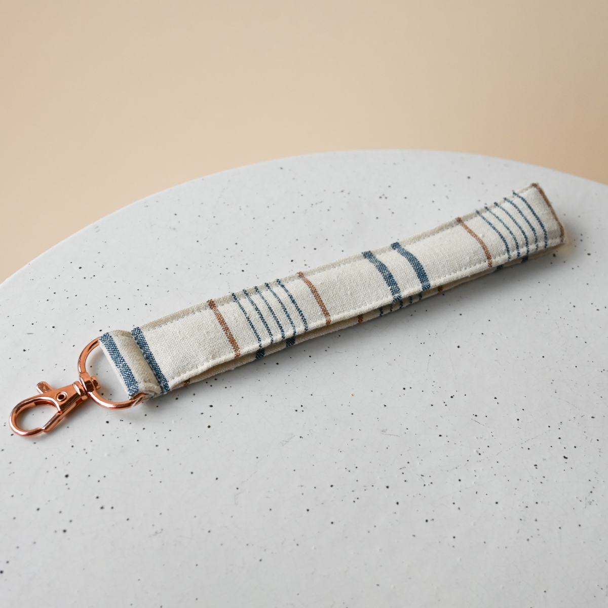 Key Fob in Lugano, a fabric wristlet strap with a rose gold clasp, cream woven chambray with blue stripes and fine rust pinstripes.