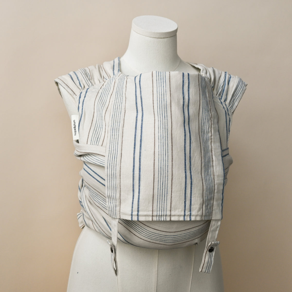 Lugano Meh Dai carrier shown on a dress form, cream woven chambray with blue stripes and fine rust pinstripes, with the hope&plum label on the strap.