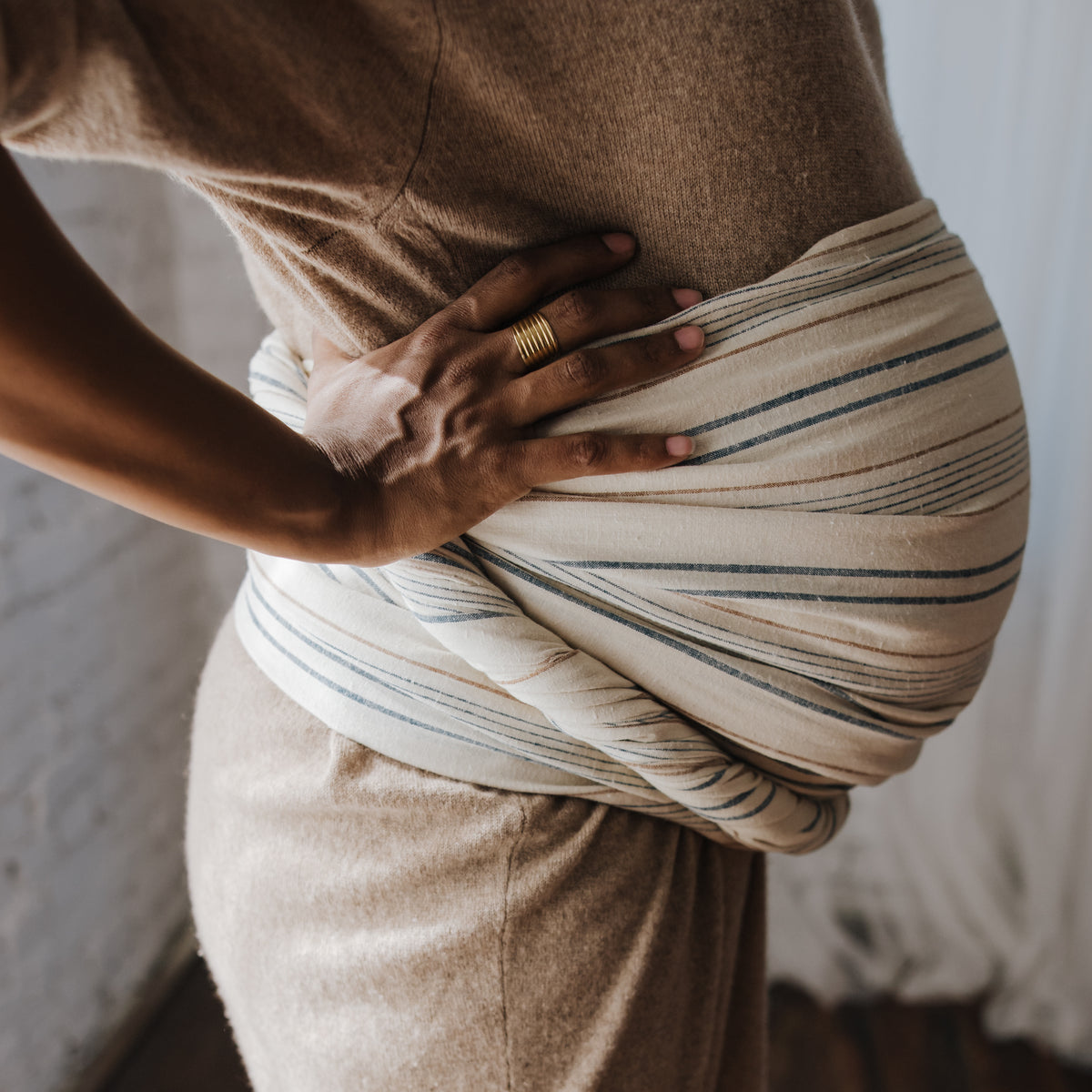 Side view of the Lugano Ring Sling wrapped around the wearer's waist and hip, showing how the woven striped chambray gathers and spreads across the body.