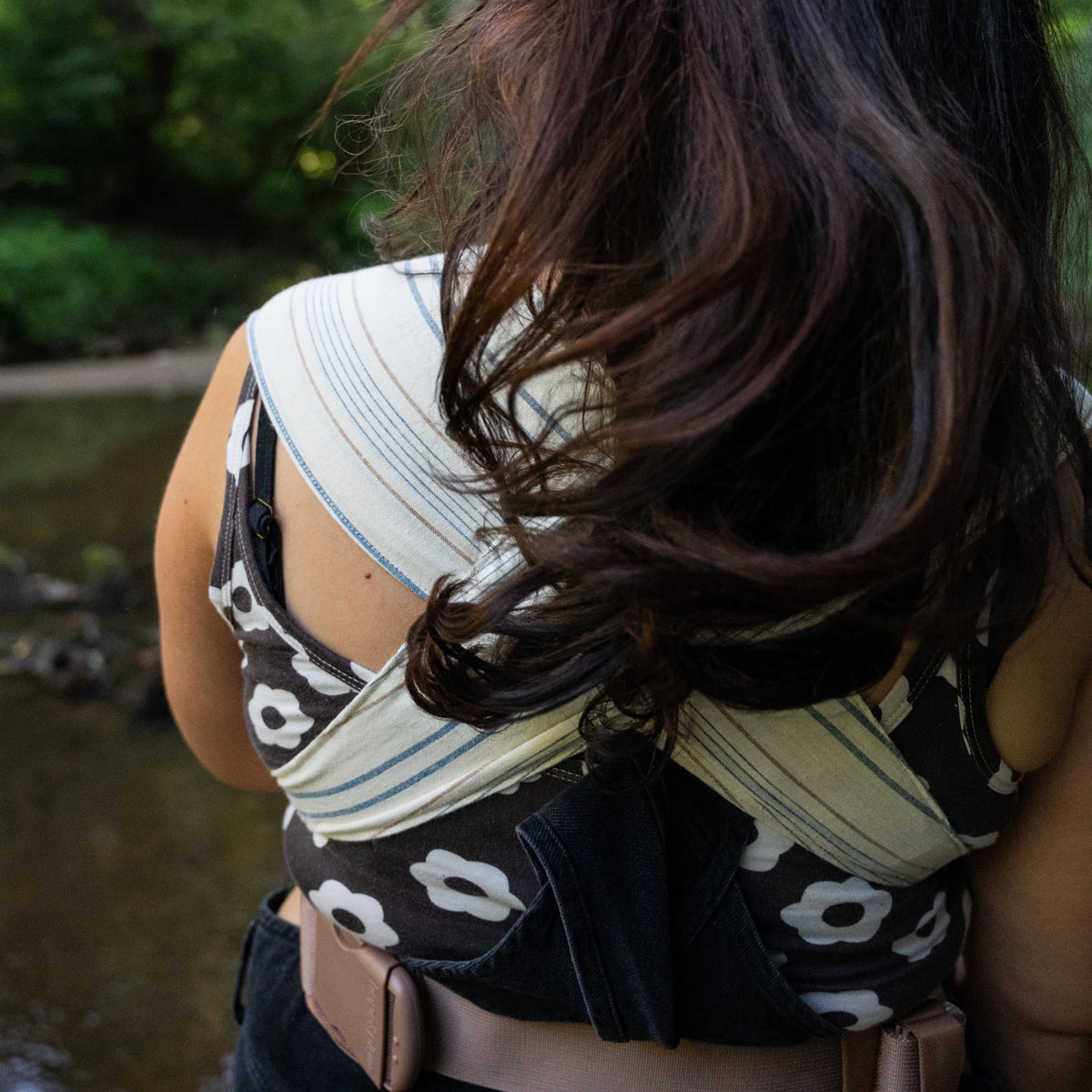 Back view of the Lugano Sprout Newborn Carrier, its striped chambray panels crossed over the shoulders above a padded buckled waistband.