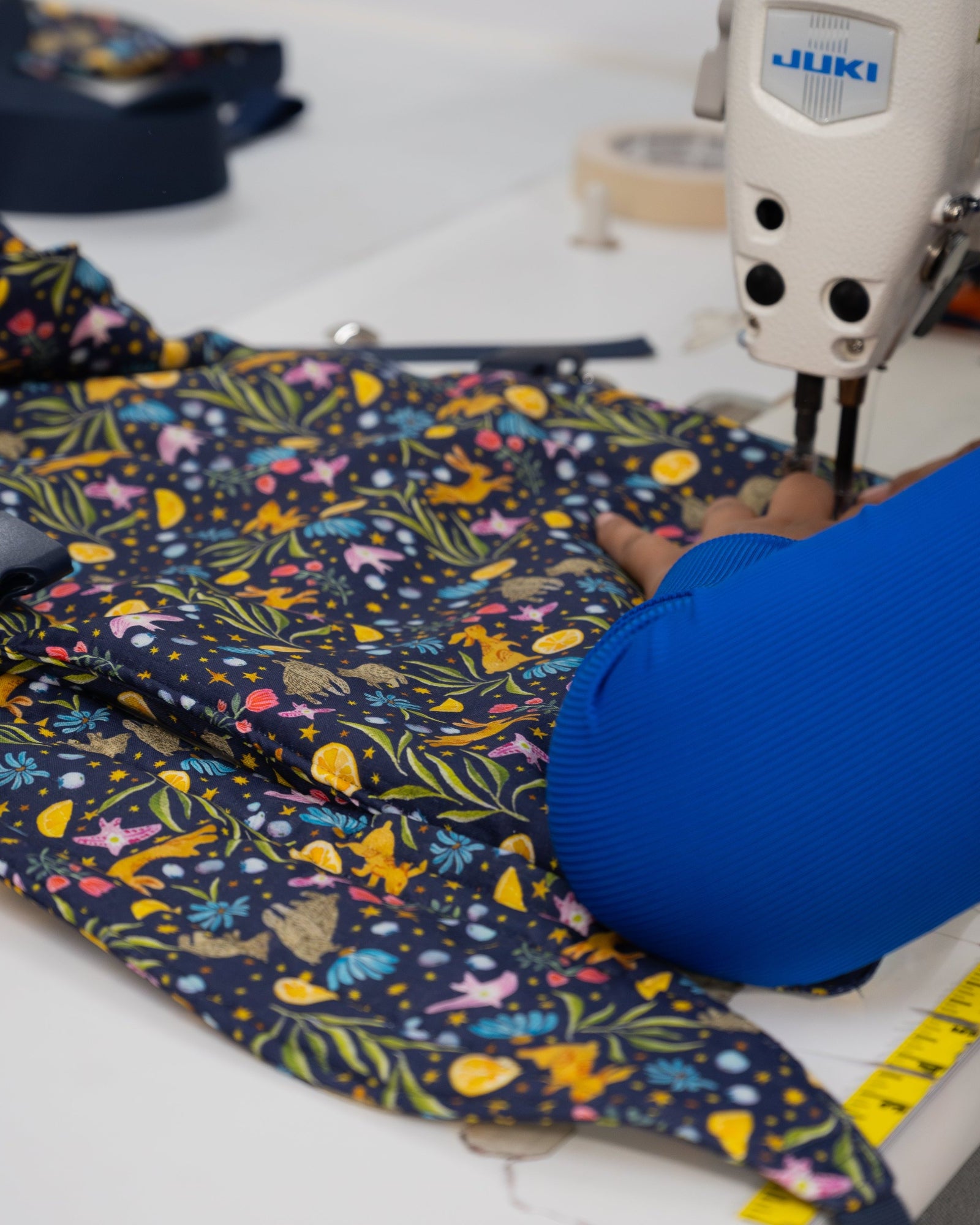 Person sewing colorful fabric with a Juki sewing machine on a white table.