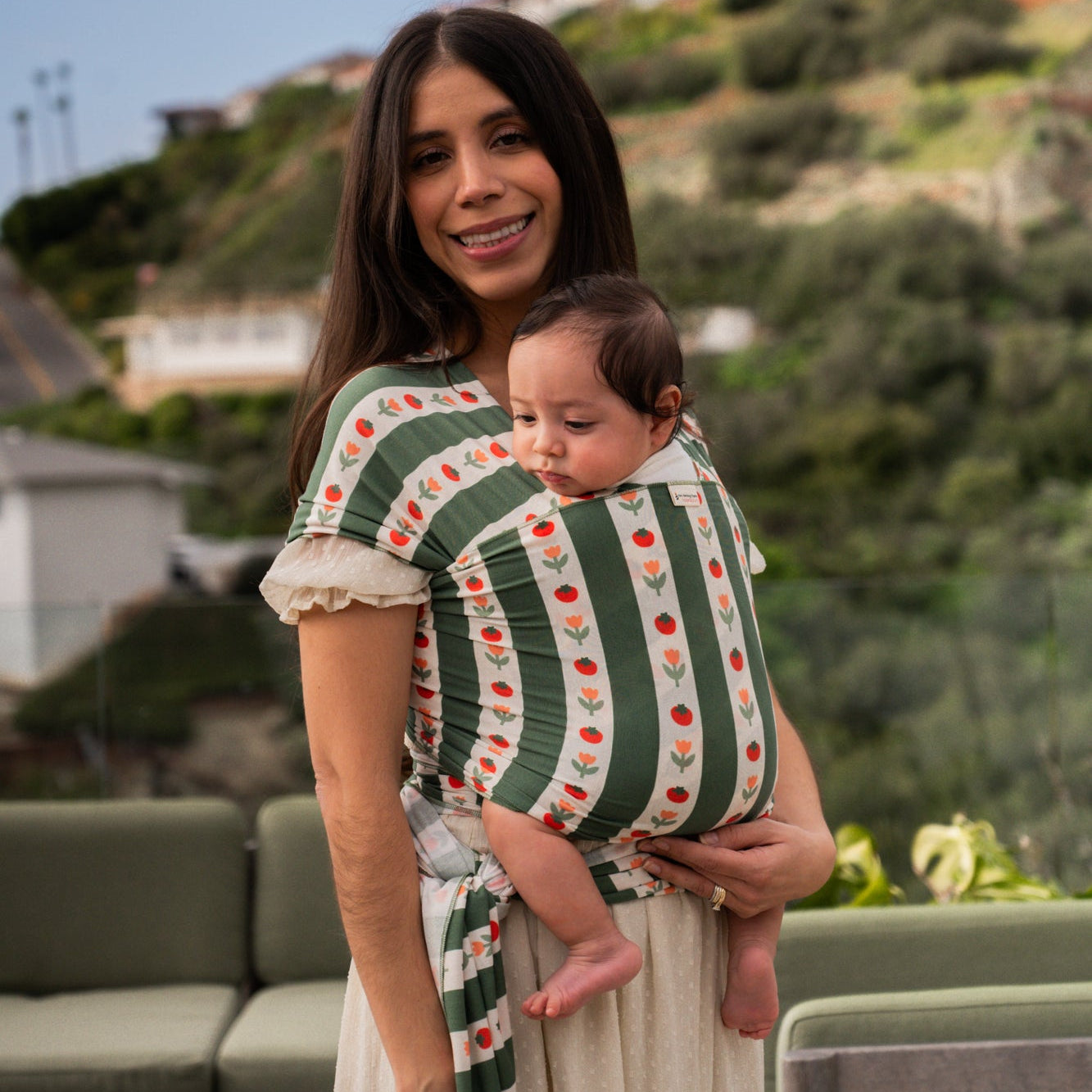 Woman holding a baby in a striped wrap with a scenic background Medley - hope&plum carriers - green and white striped carrier with tomatoes and tulips on the white stripe