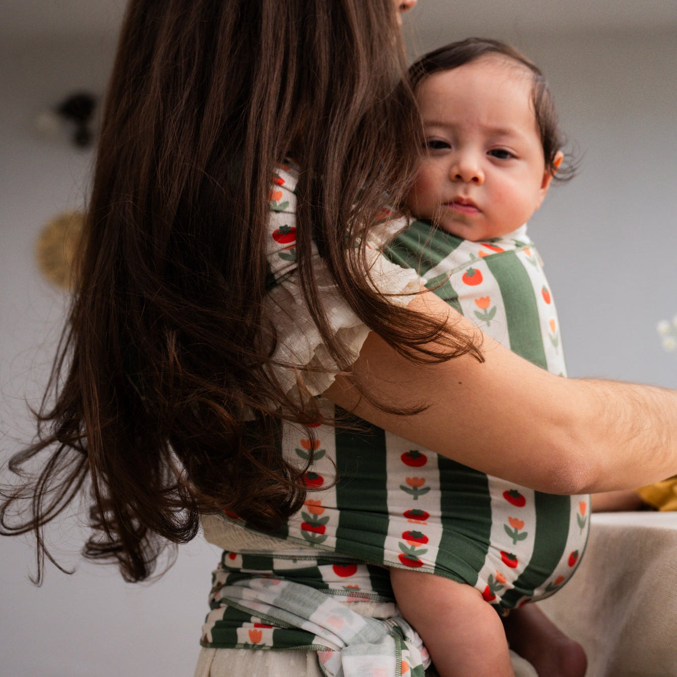 Woman holding a baby wrapped in a floral striped wrap with a neutral background - Medley - hope&plum carriers - green and white striped carrier with tomatoes and tulips on the white stripe