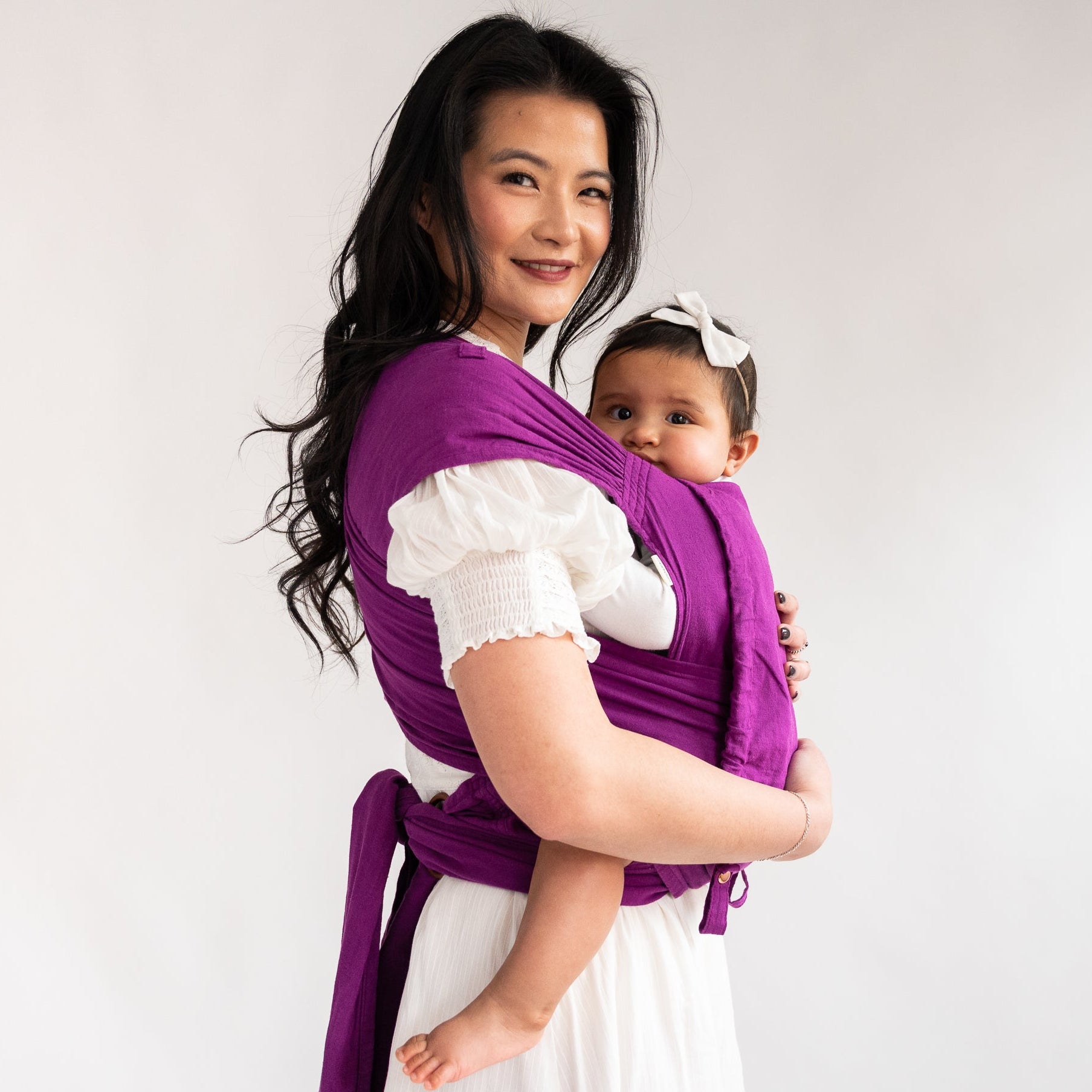 Woman holding a baby in a purple wrap meh dai against a white background