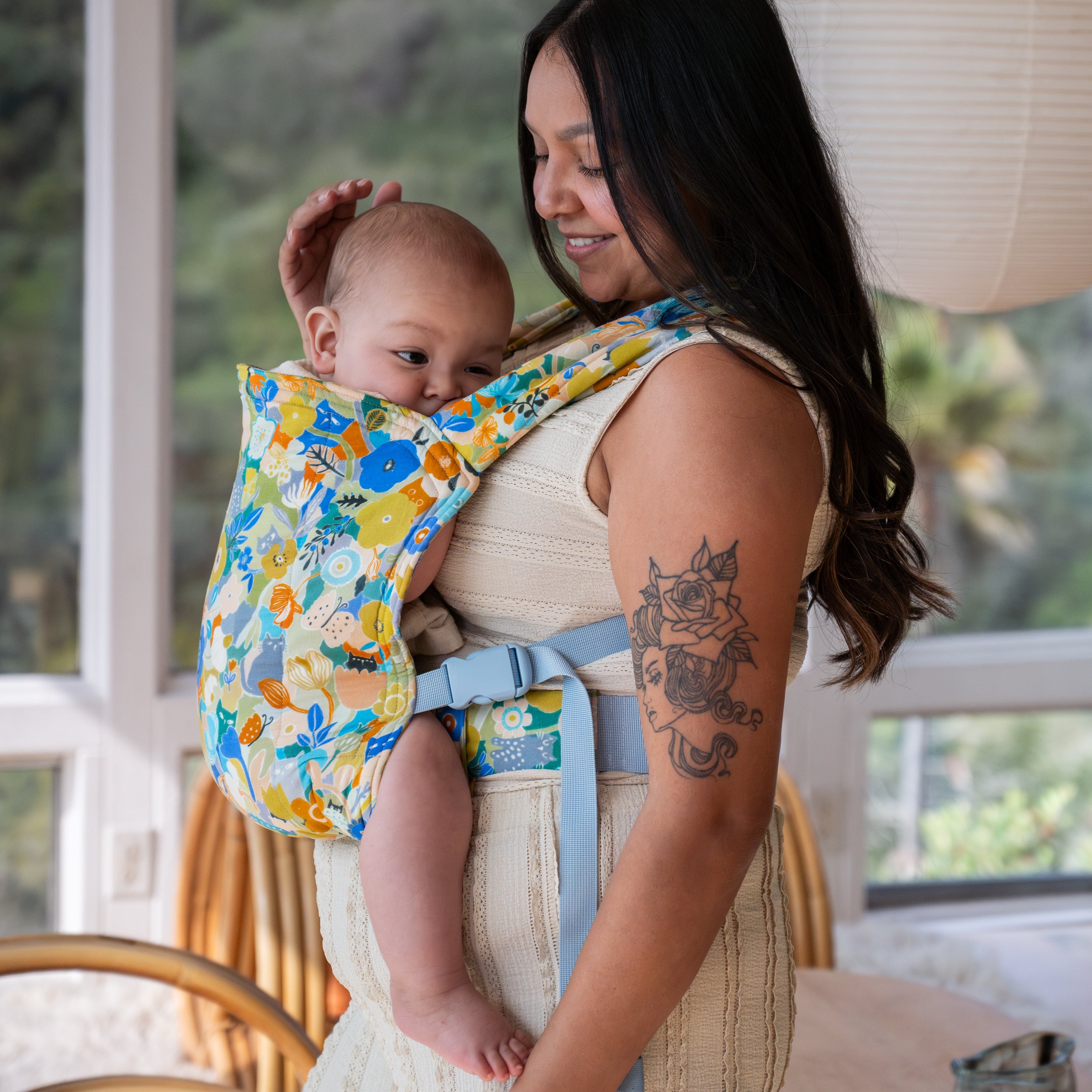 Woman holding a baby in a floral baby buckle carrier indoors