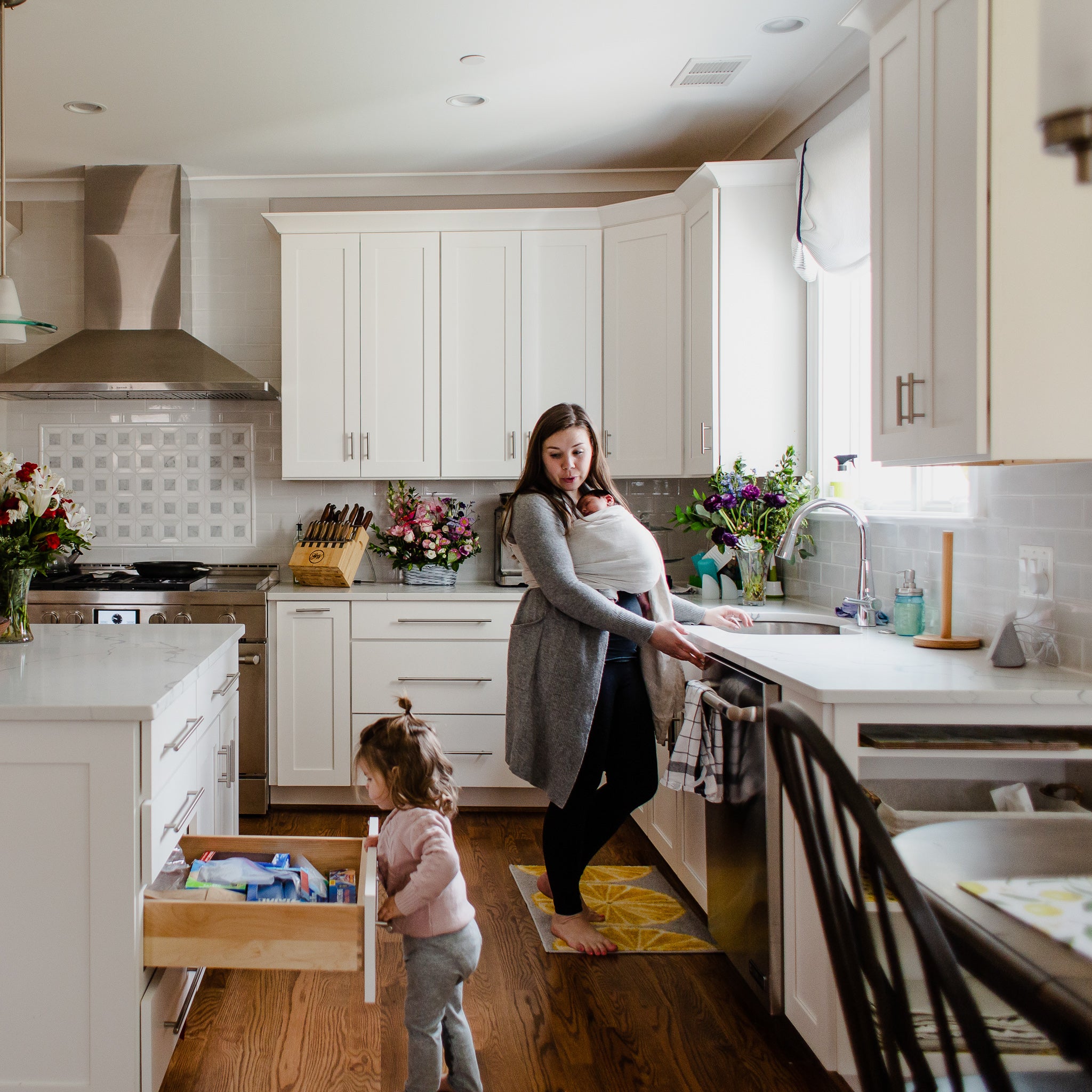 Mother using gray baby wrap carrier with her newborn while doing dishes.