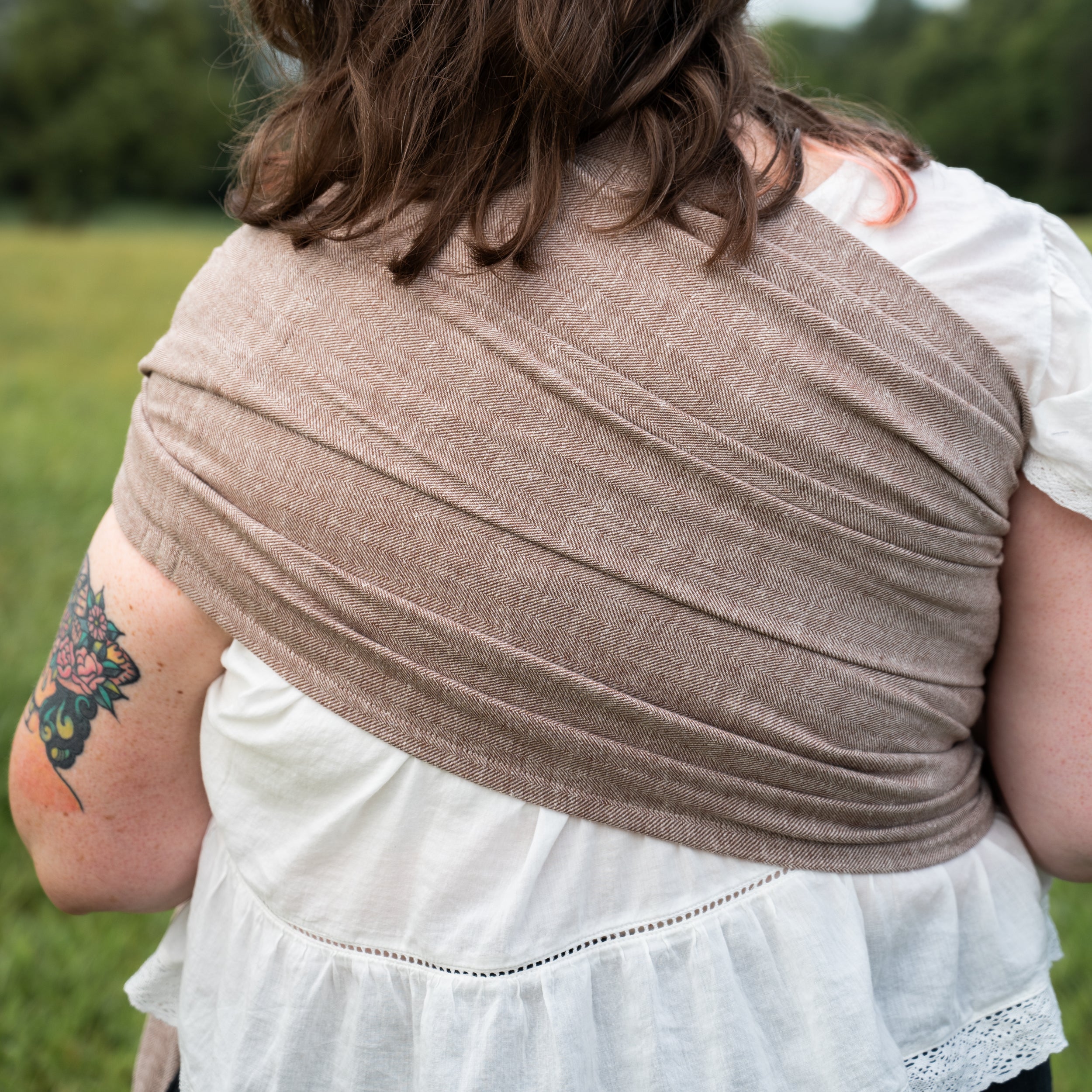 Back view close-up of the Oak Ring Sling's chocolate and oatmeal herringbone weave draped across a woman's shoulder and back.