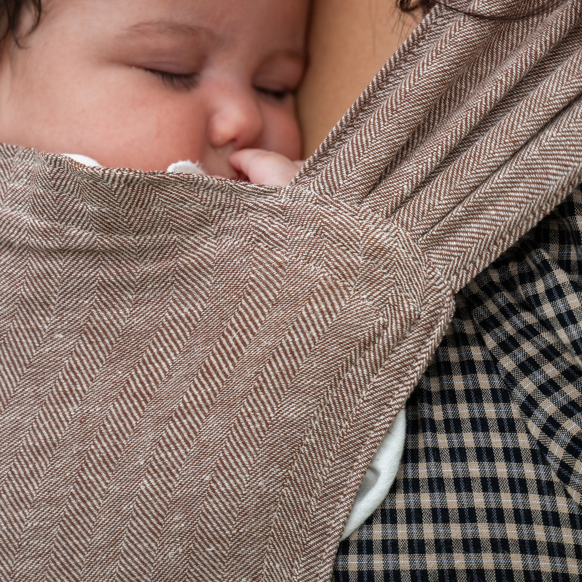 Close-up of a sleeping newborn's face tucked into the Oak Sprout Newborn Carrier's chocolate and oatmeal herringbone weave.
