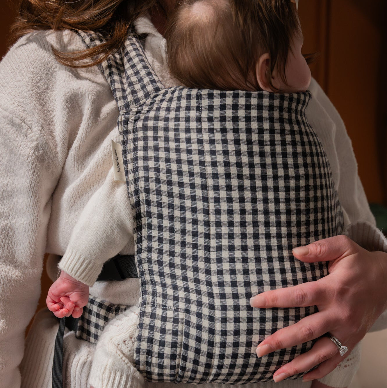 Person holding a baby in a checkered baby carrier indoors.