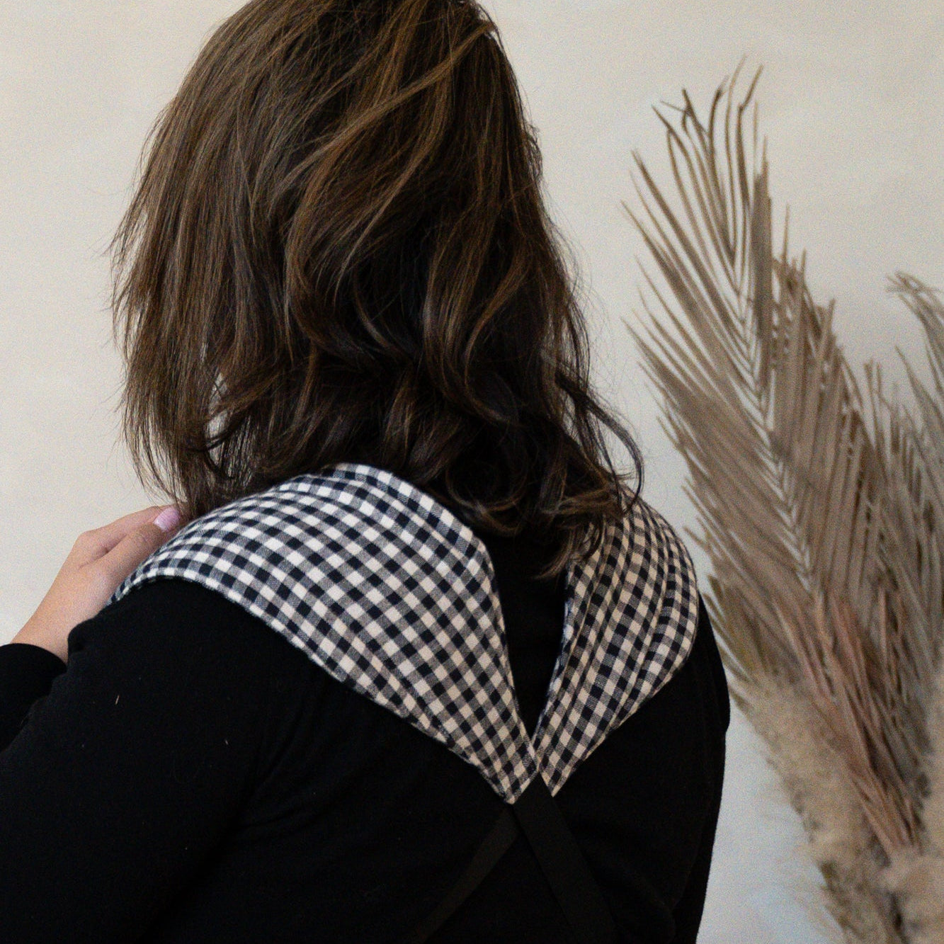 Person wearing a black shirt with a checkered baby carrier against a neutral background
