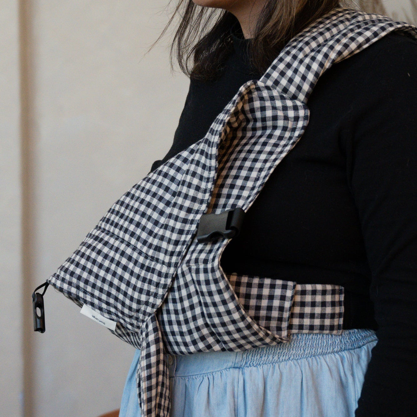 Person wearing a black and white gingham baby carrier with a plain background