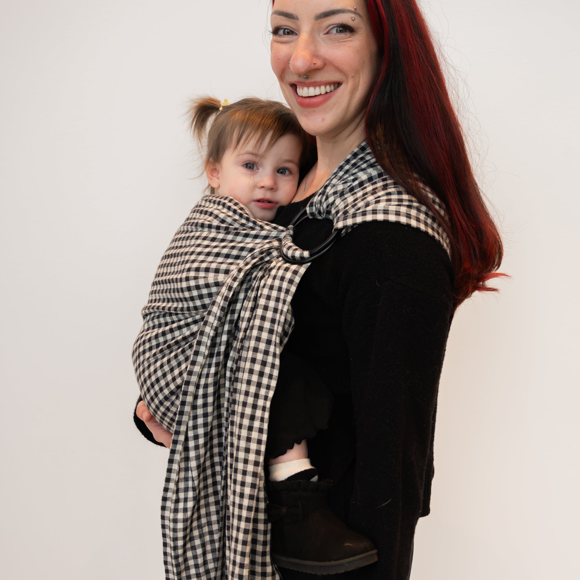 Woman holding a baby in a black and white gingham patterned ring sling