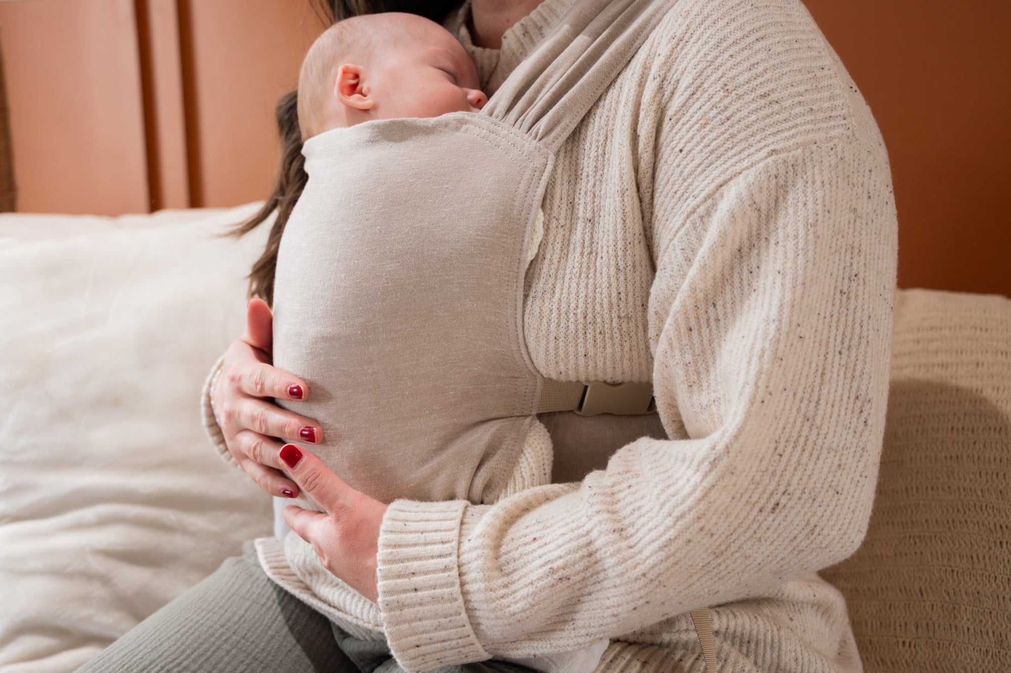 Woman holding her newborn in a beige carrier on an orange wall