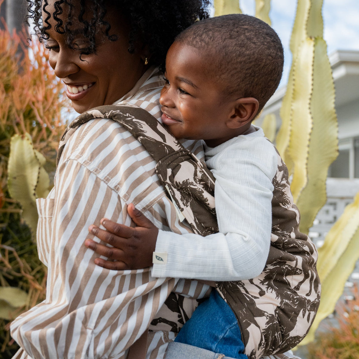 Lark Kid Carrier in Rodeo β caregiver and toddler smiling together, toddler riding in the mustang print back carrier.