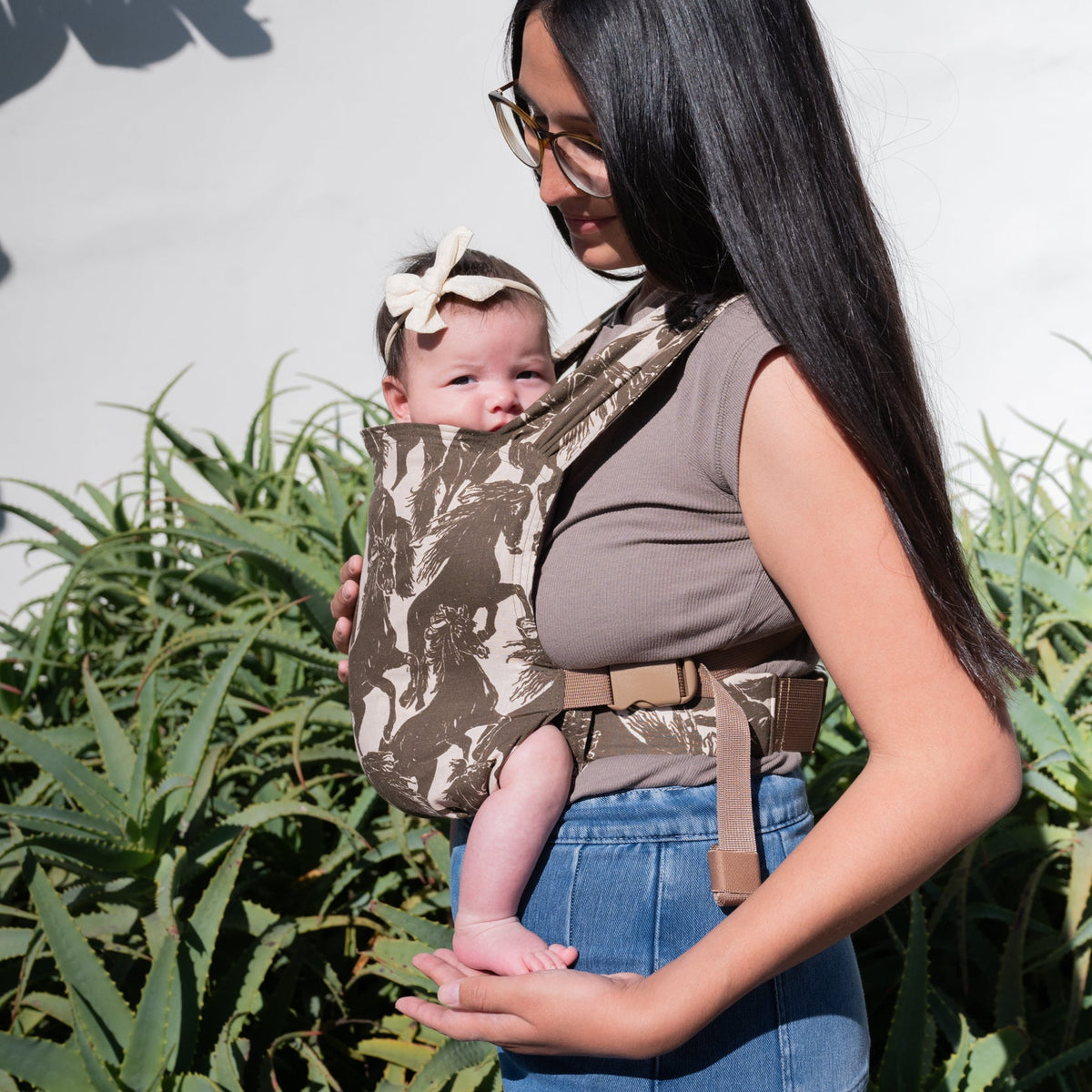 Sprout Newborn Carrier in Rodeo — side profile of a caregiver holding a newborn in the mustang print carrier.