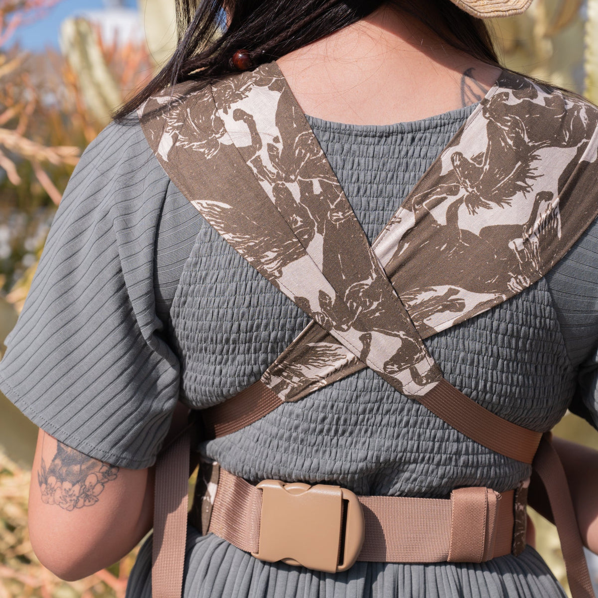 Sprout Newborn Carrier in Rodeo — back view of the crossed straps in the mustang print, caregiver in a straw hat.