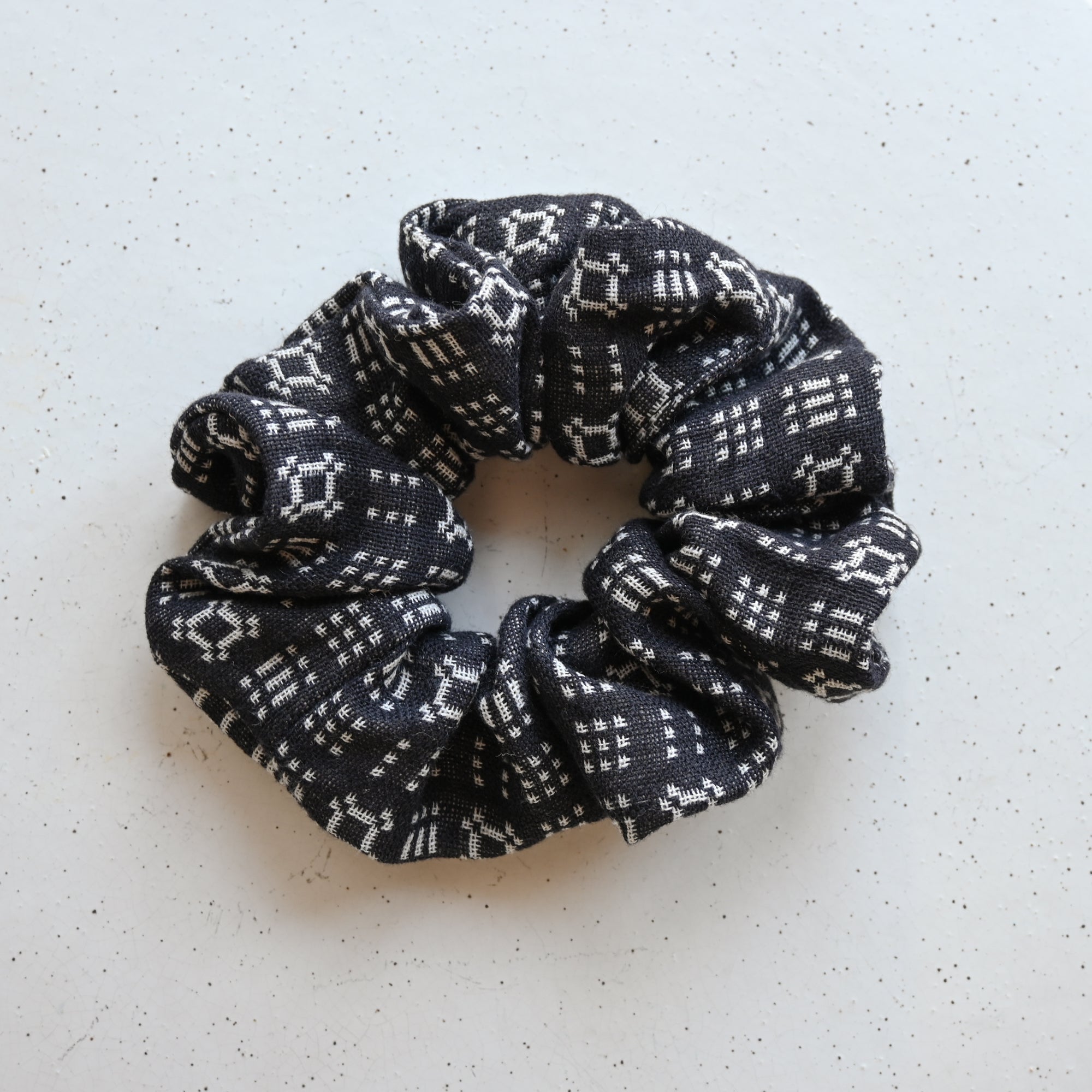 A single oversized scrunchie in dark navy woven fabric with a cream geometric pattern of diamond and cross motifs in a folk or jacquard-style weave.
