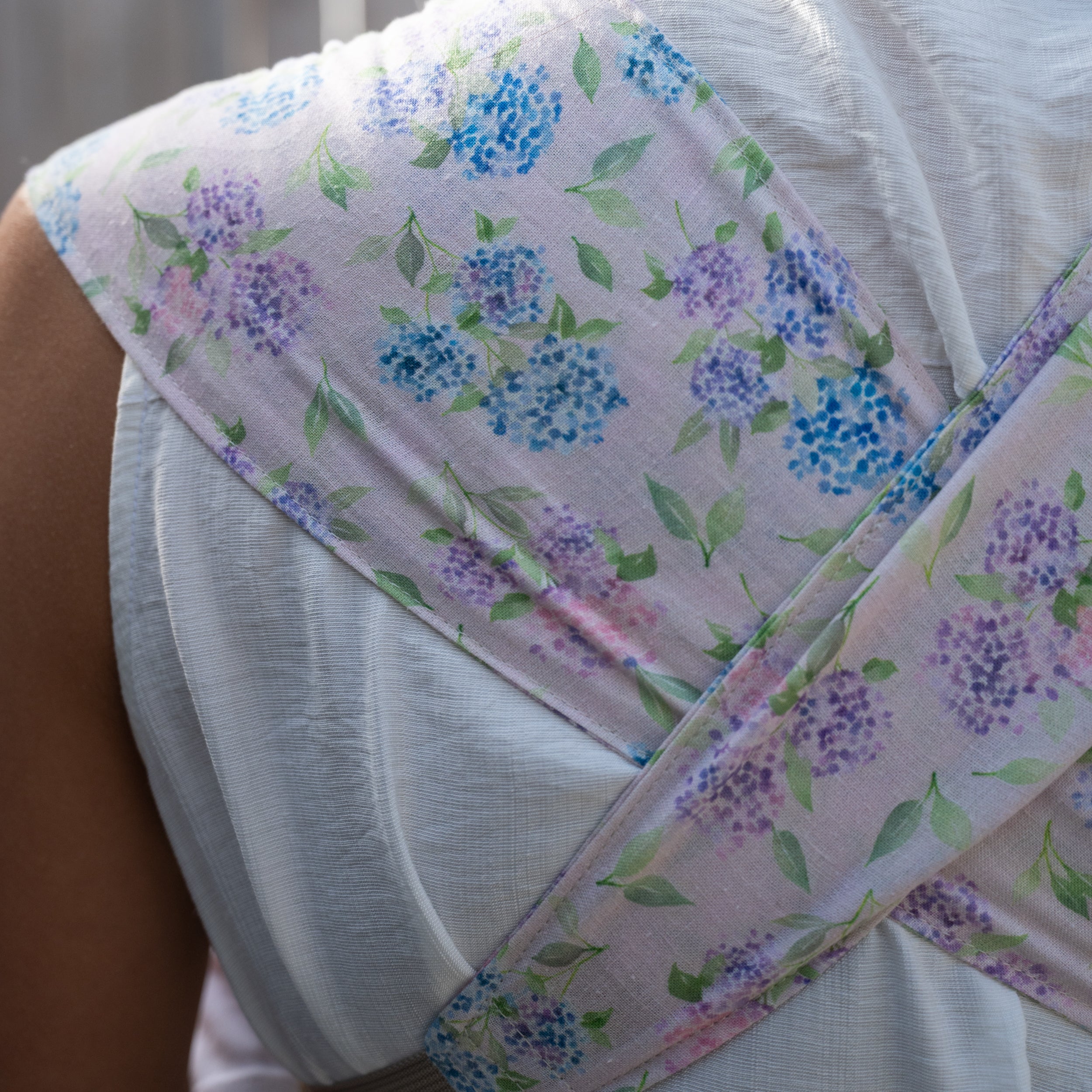 Sprout Newborn Carrier in Blush — close-up of the crossed back straps in the blue and lavender hydrangea print on a soft pink background.