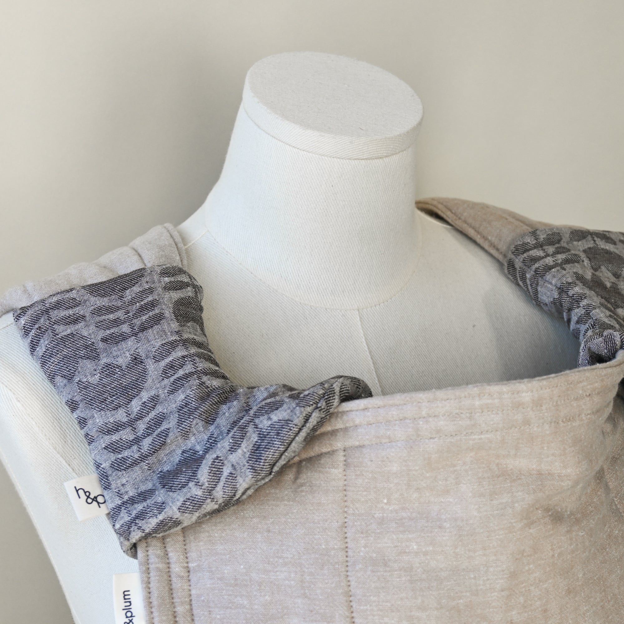 Mannequin wearing a beige carrier with gray tulip drool pads, on a plain background.