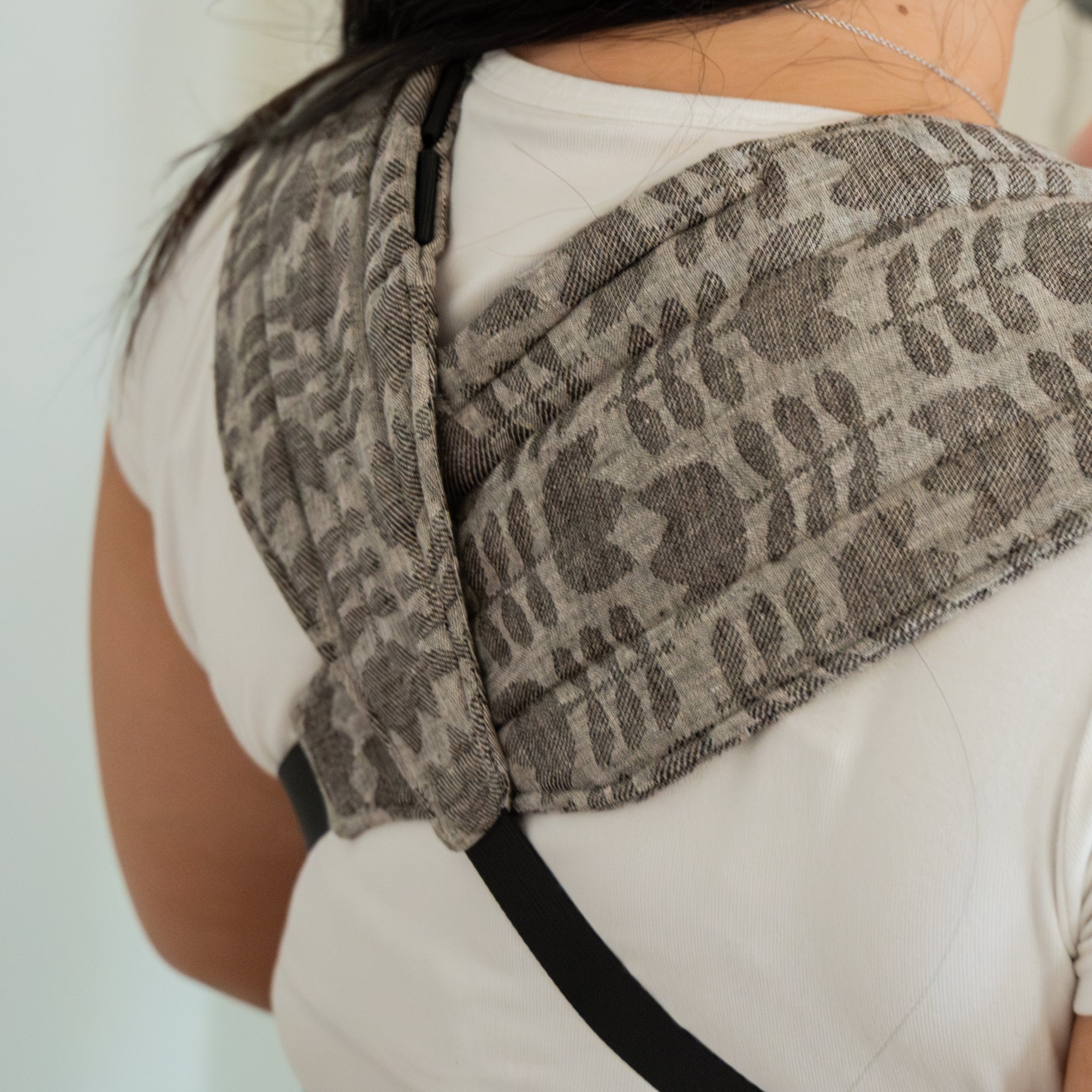 Person wearing a grey tulip patterned baby carrier with a neutral background