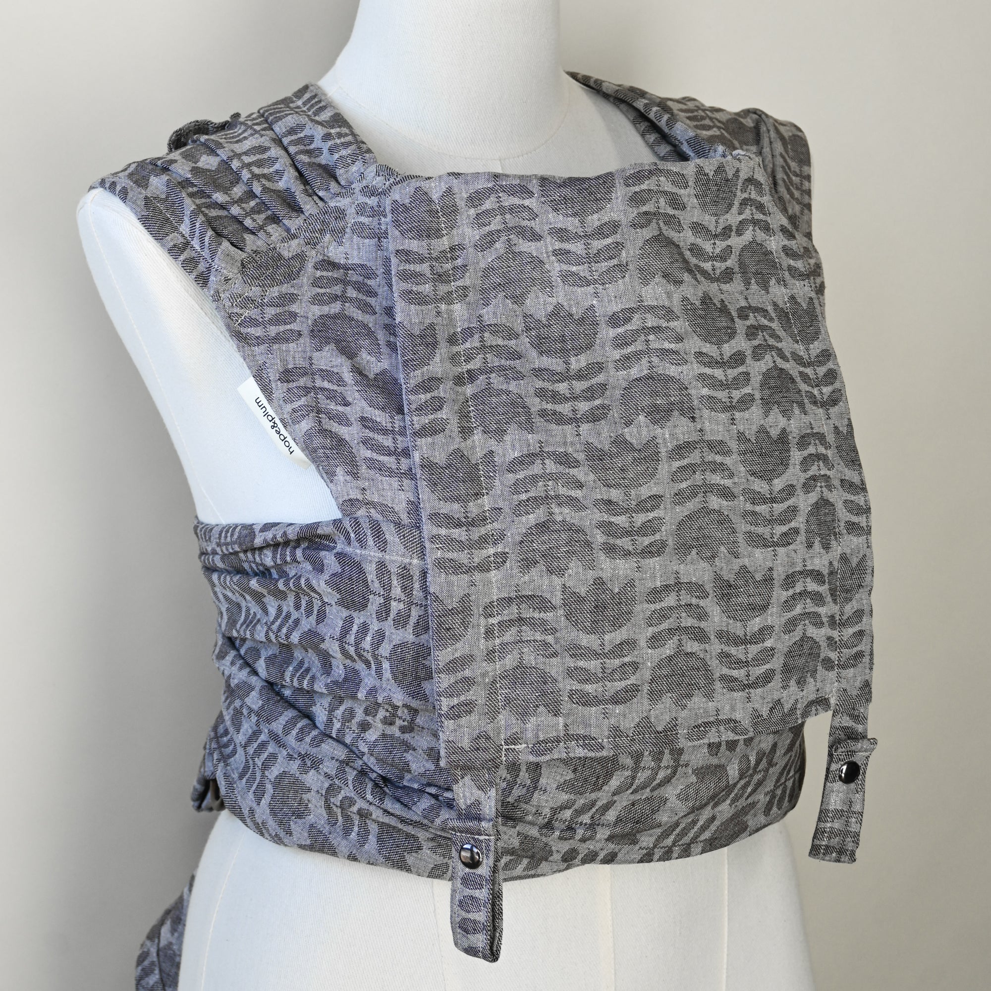 Gray tulip patterned baby carrier on a mannequin against a plain background
