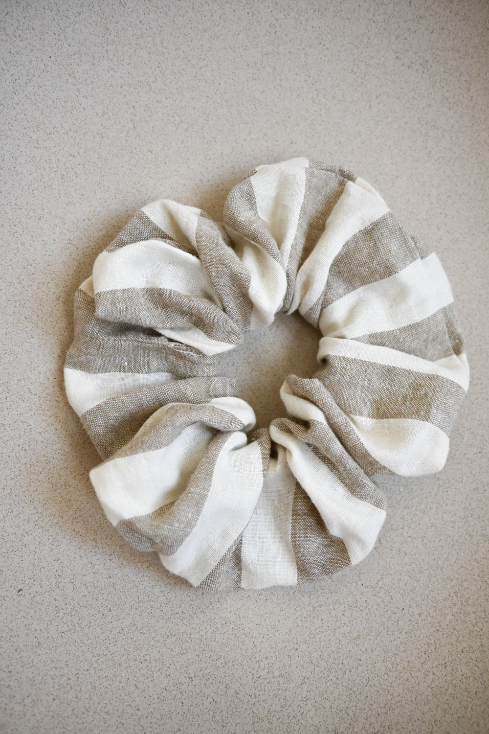 A single oversized scrunchie in natural and white wide-stripe woven fabric.