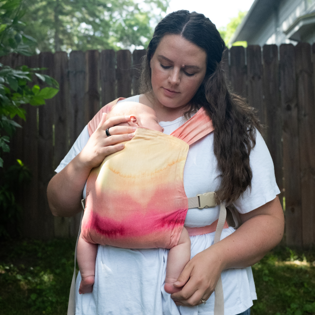 Almost Perfect Sprout Newborn Carrier in Vesper — parent babywearing a newborn, watercolor sunset gradient panel