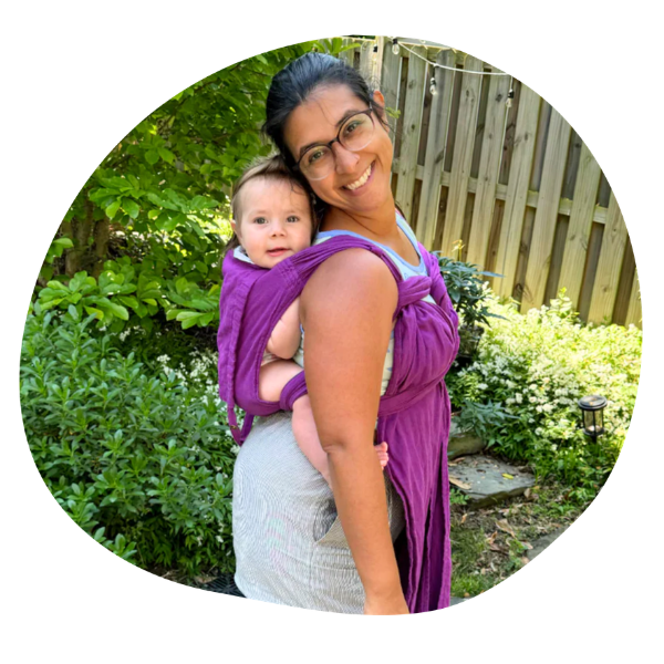 woman with black hair and glasses holding a baby in a purple meh dai carrier on her back