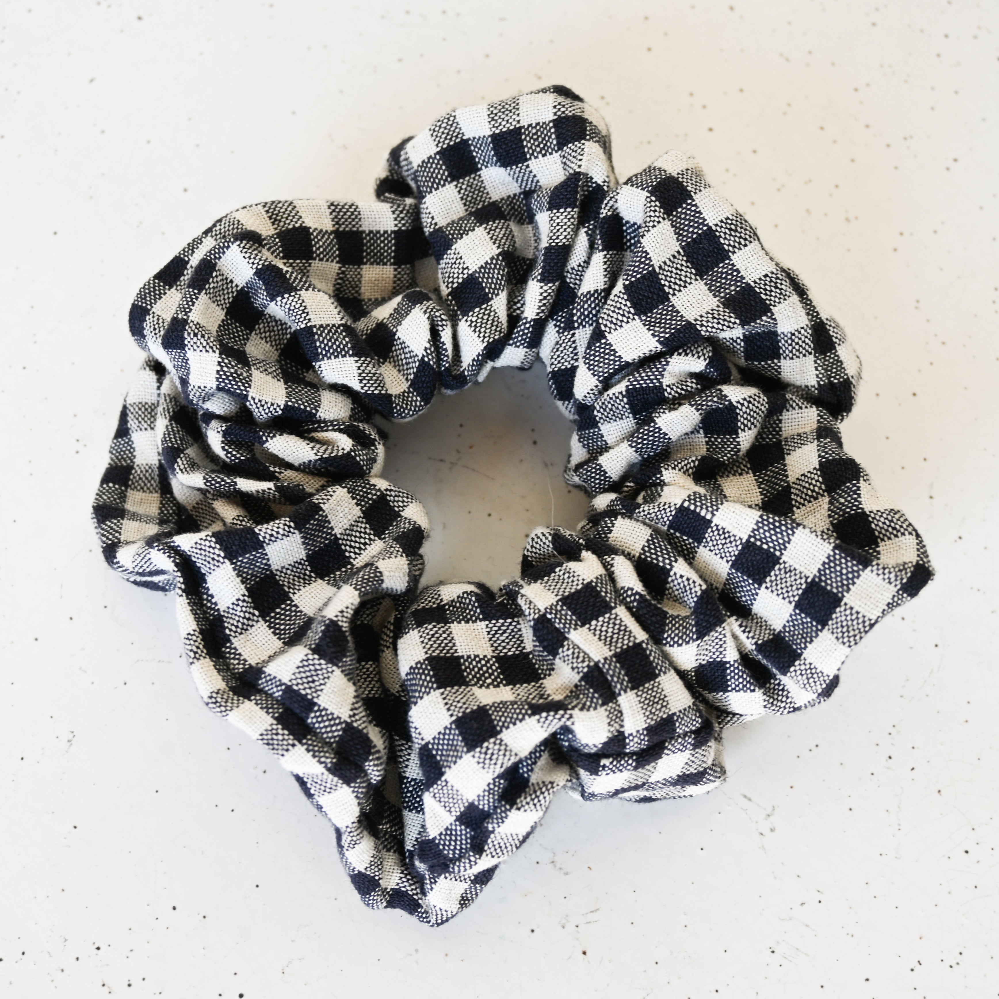 A single oversized scrunchie in a navy and cream gingham check woven fabric.