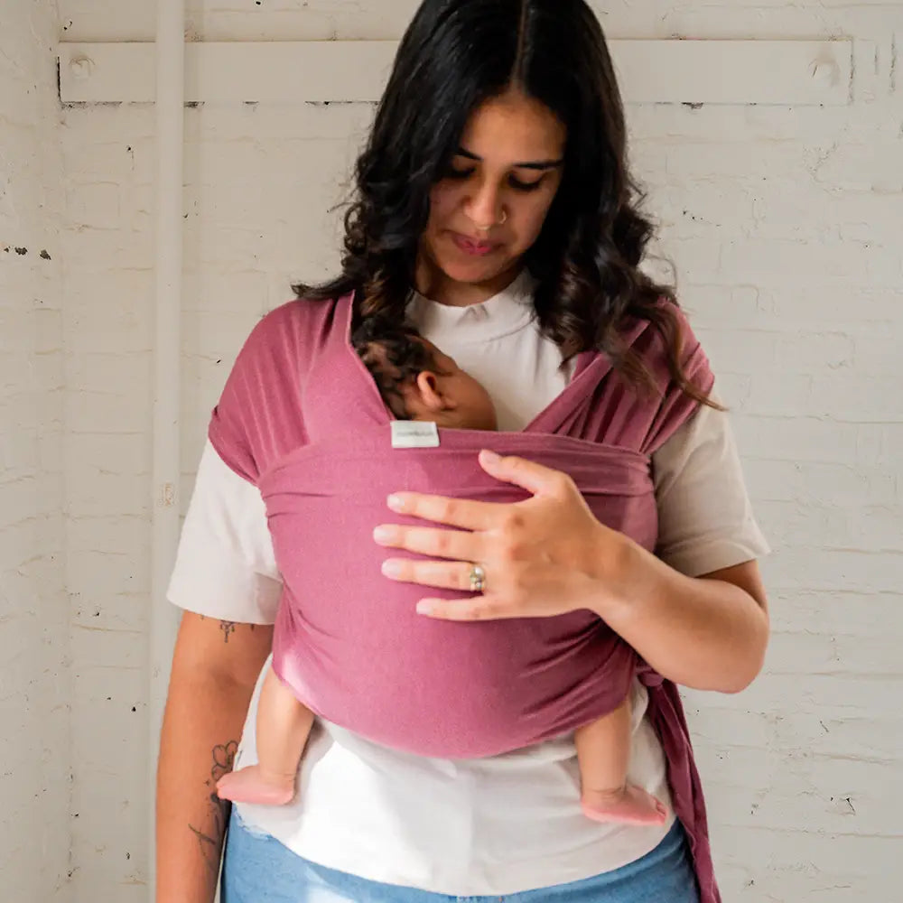 Mother holding newborn baby in rose colored baby wrap 