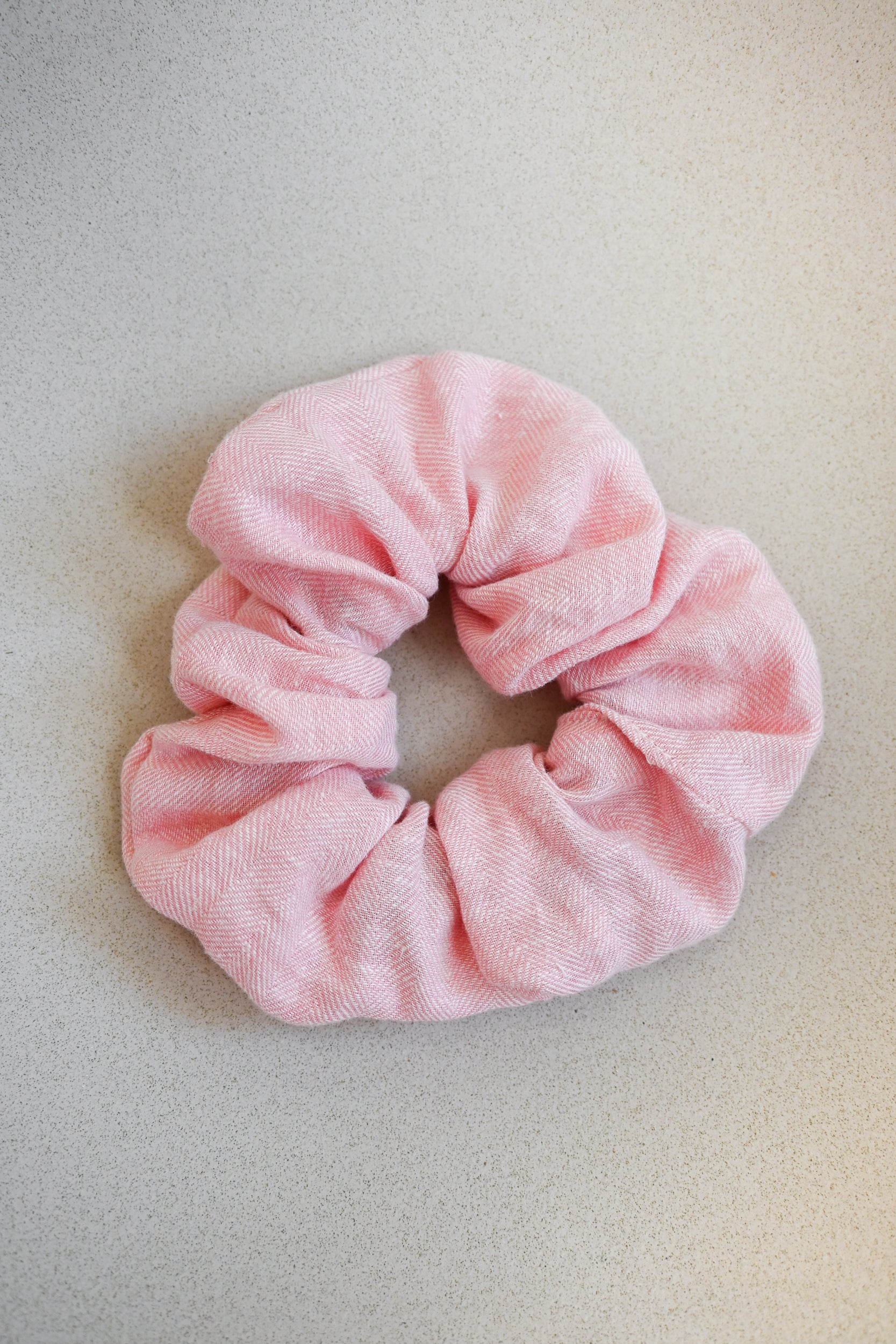 A single oversized scrunchie in pale blush pink woven fabric with a subtle herringbone texture.