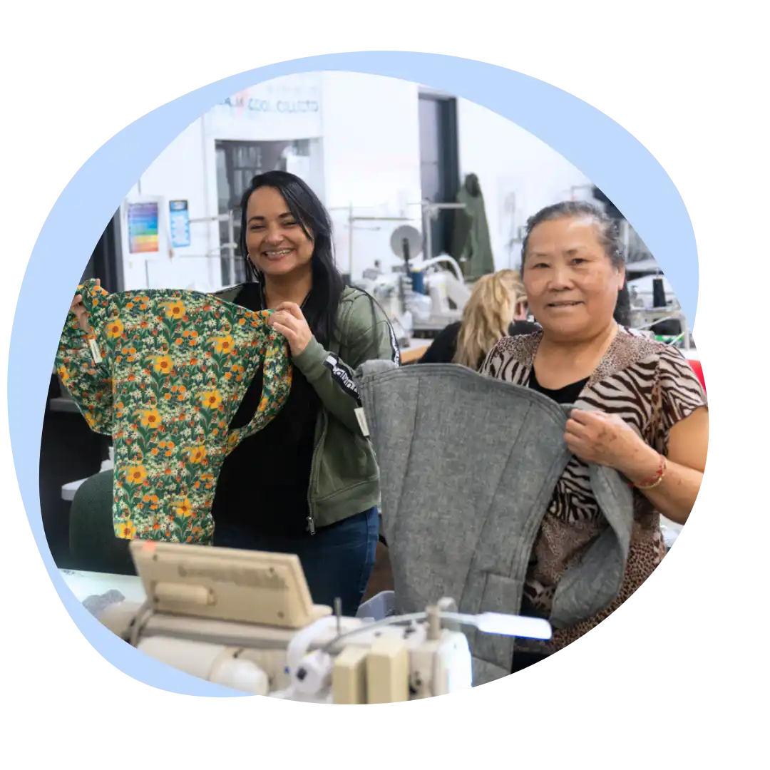 Two women holding up baby carriers that they’ve sewn while smiling.