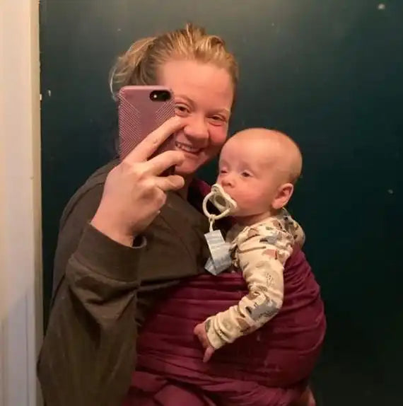 Woman holding baby in carrier taking selfie.