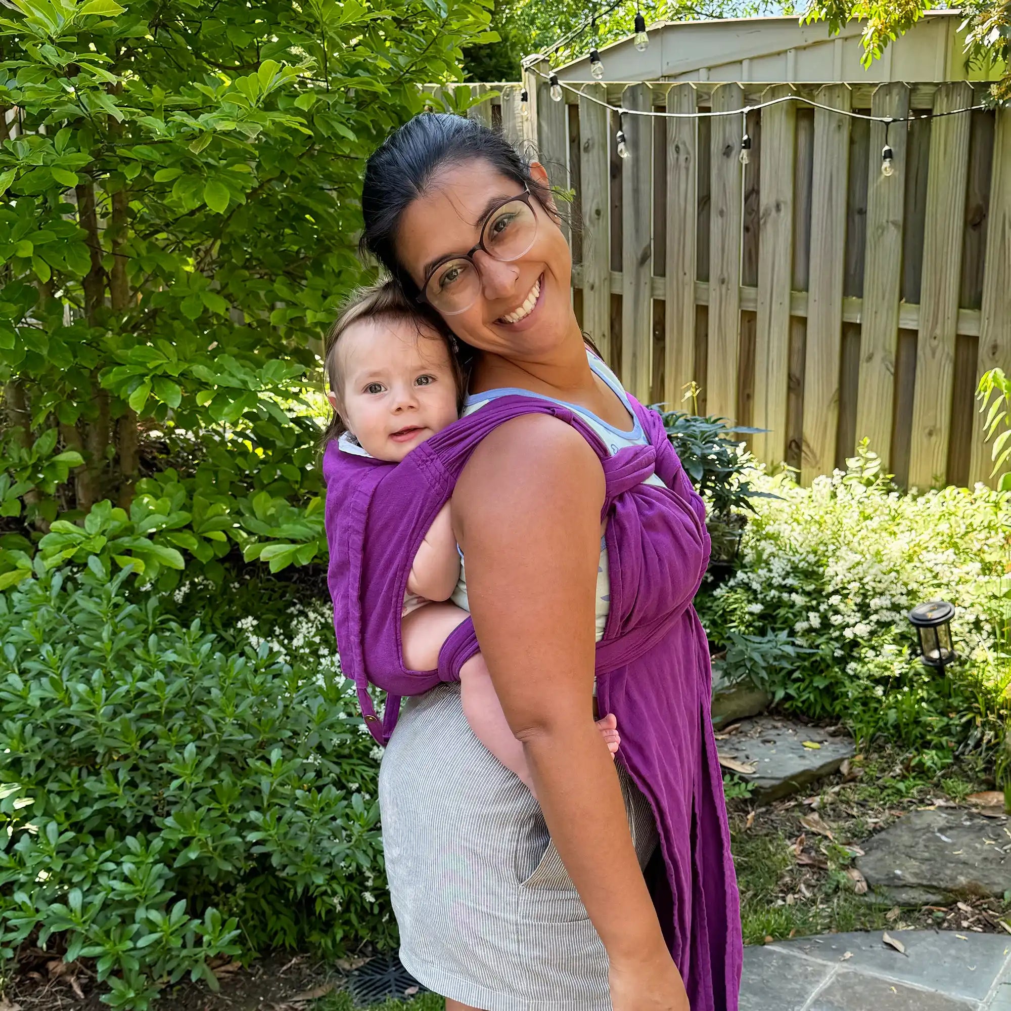 Woman carrying baby in purple wrap.