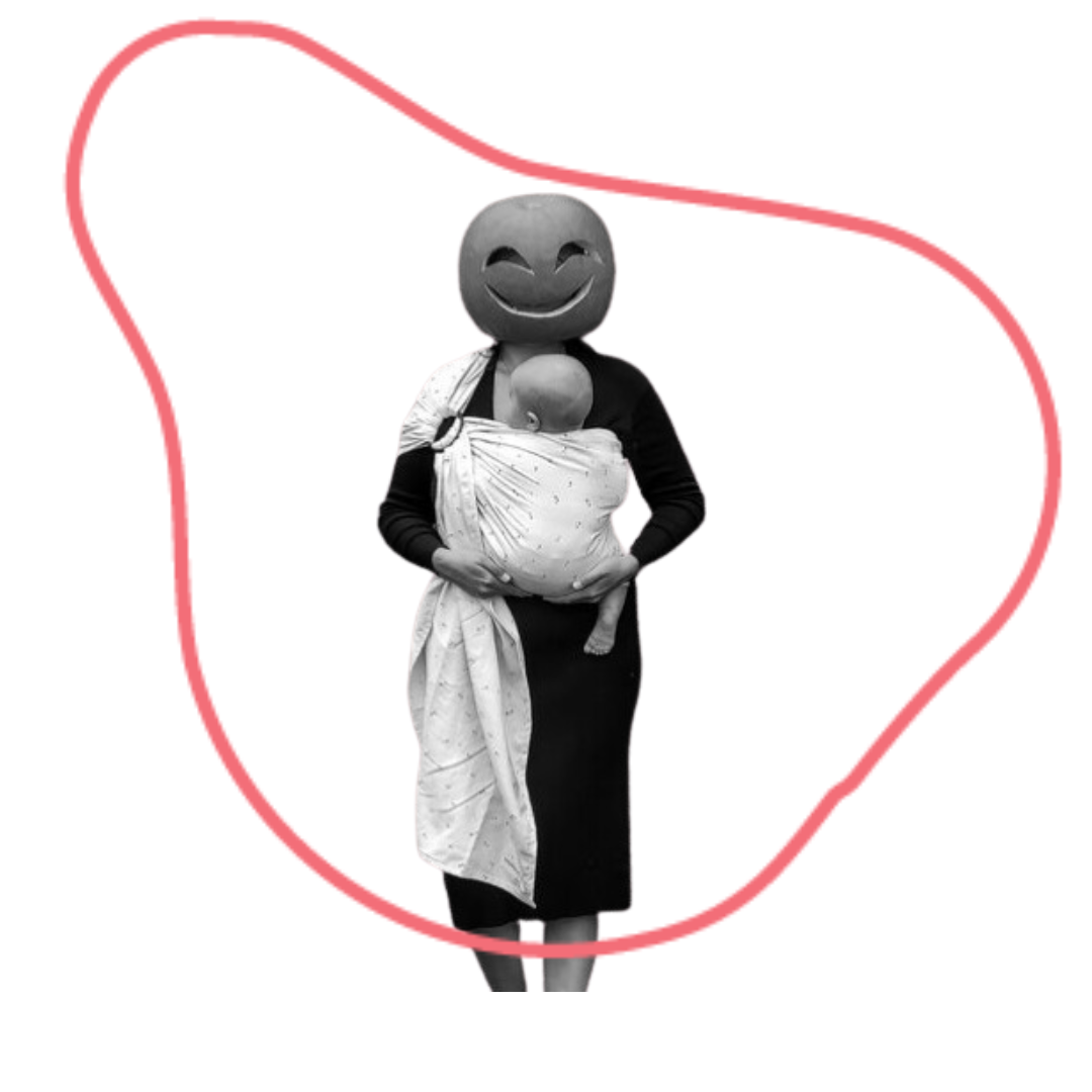 Black and white photo of a person dressed in black and wearing a baby in a ring sling. The adult has a pumpkin over their head that has been carved into a smiling face.