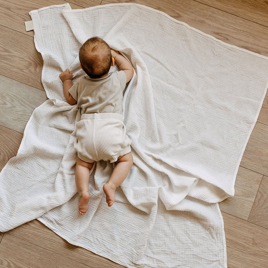 Baby practicing tummy time on floor with white blanket
