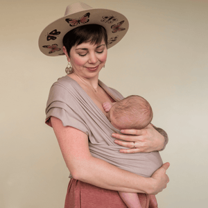 A white straight size woman nurses her baby while supporting them worn in a hope&plum fawn baby wrap